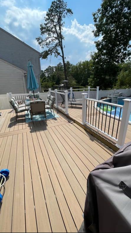 A wooden deck with a table and chairs and a pool in the background.