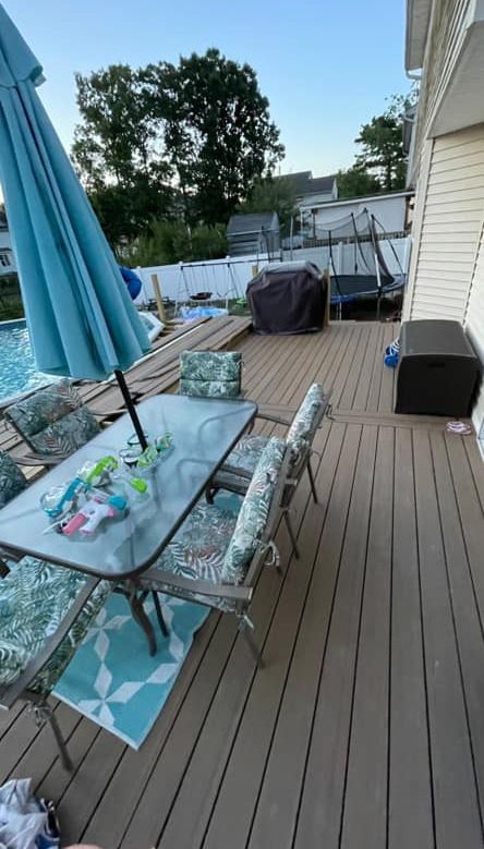 A deck with a table and chairs and an umbrella next to a pool.