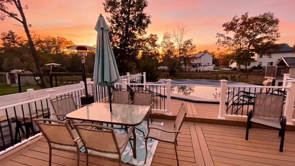 A deck with a table and chairs and an umbrella at sunset.