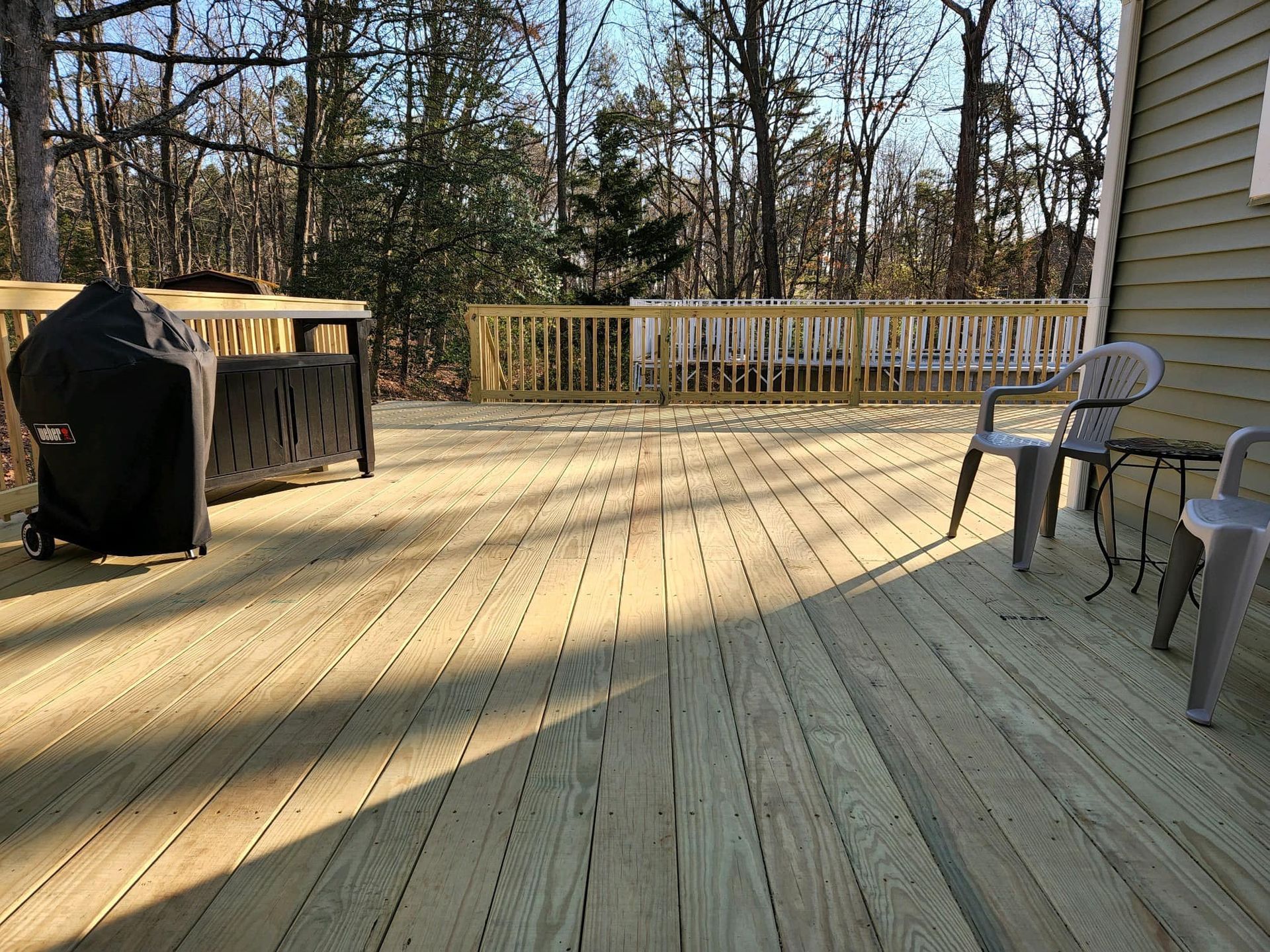 A wooden deck with chairs and a grill on it.