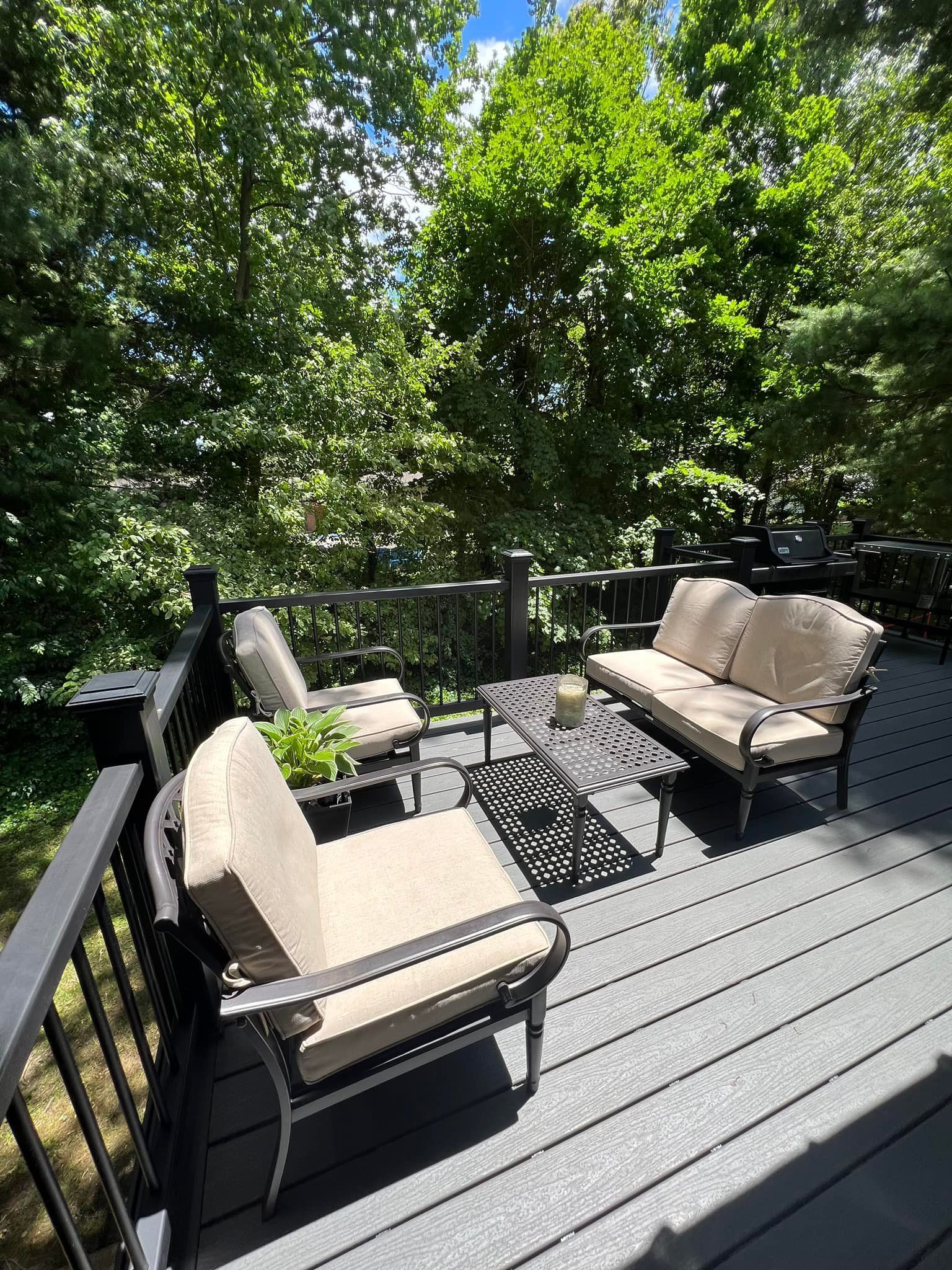 A deck with a couch and chairs on it surrounded by trees.