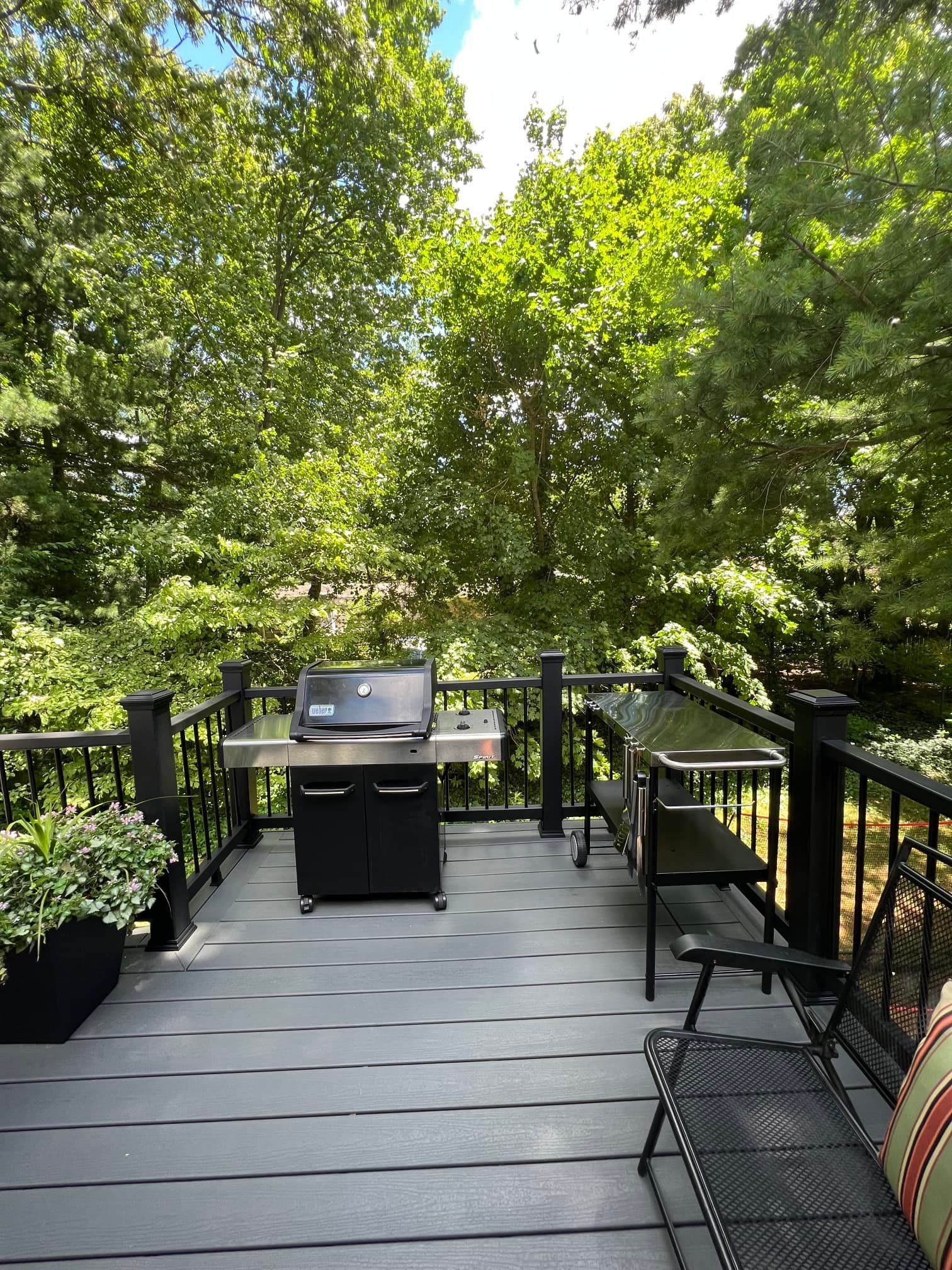 There is a grill on the deck with trees in the background.