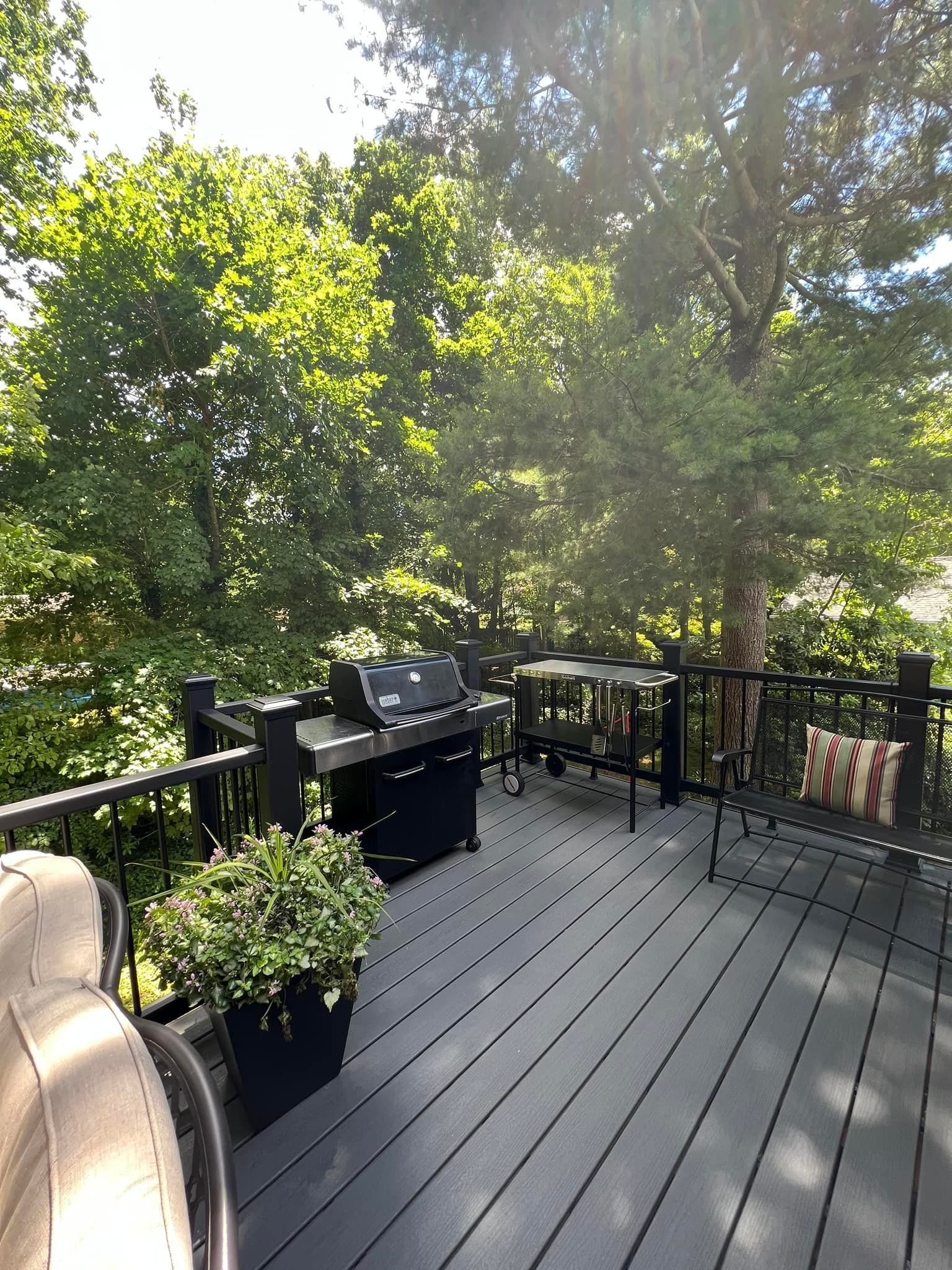 There is a grill on the deck with a view of the trees.