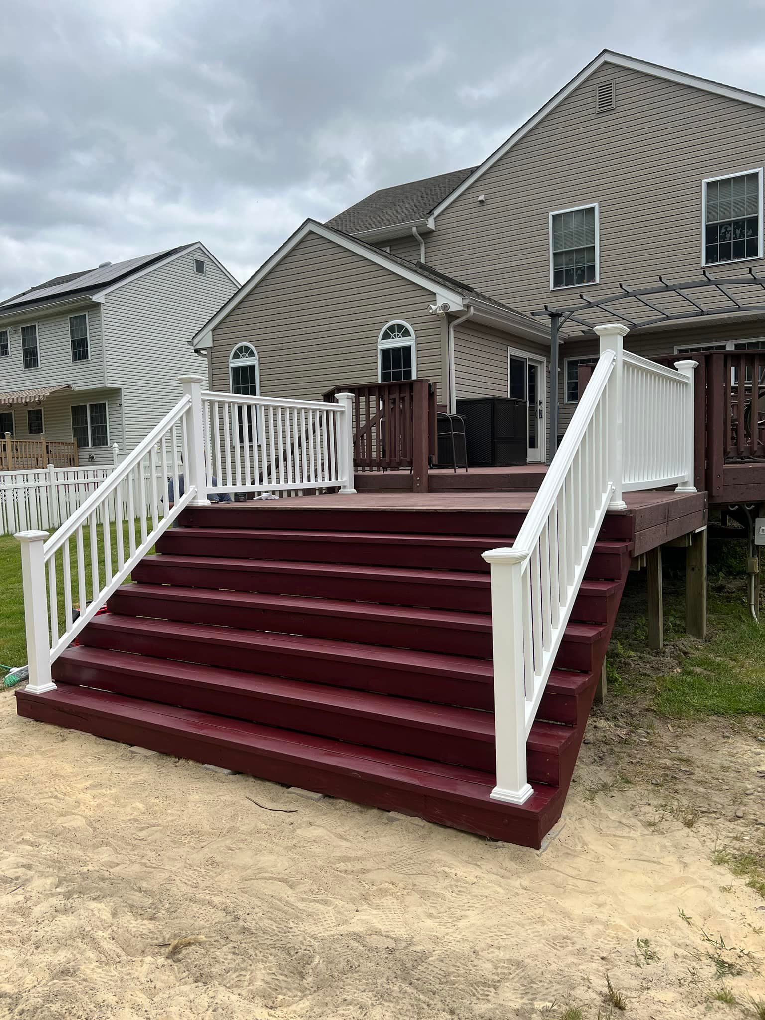 A deck with red stairs and a white railing in front of a house.