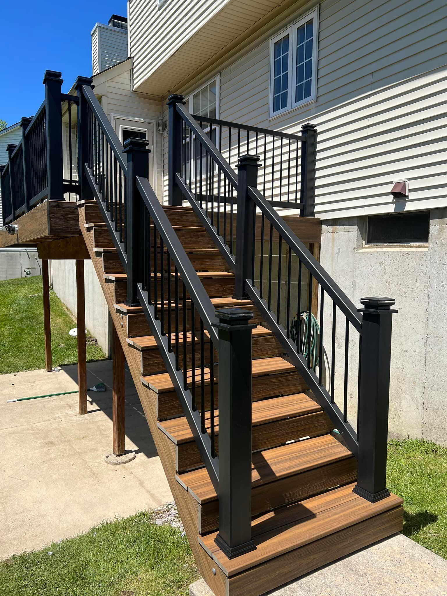 A deck with stairs leading up to it and a black railing.