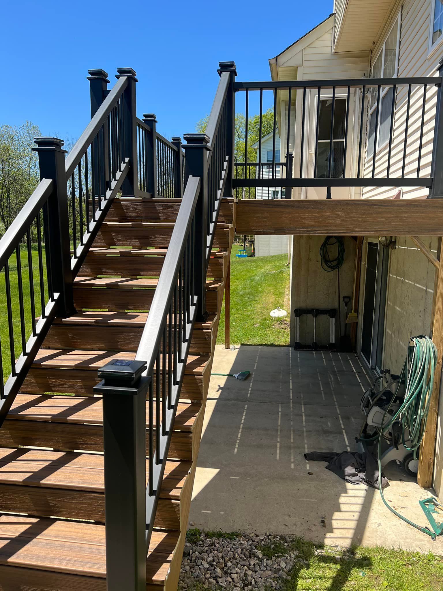 A wooden deck with stairs leading up to it and a black railing.