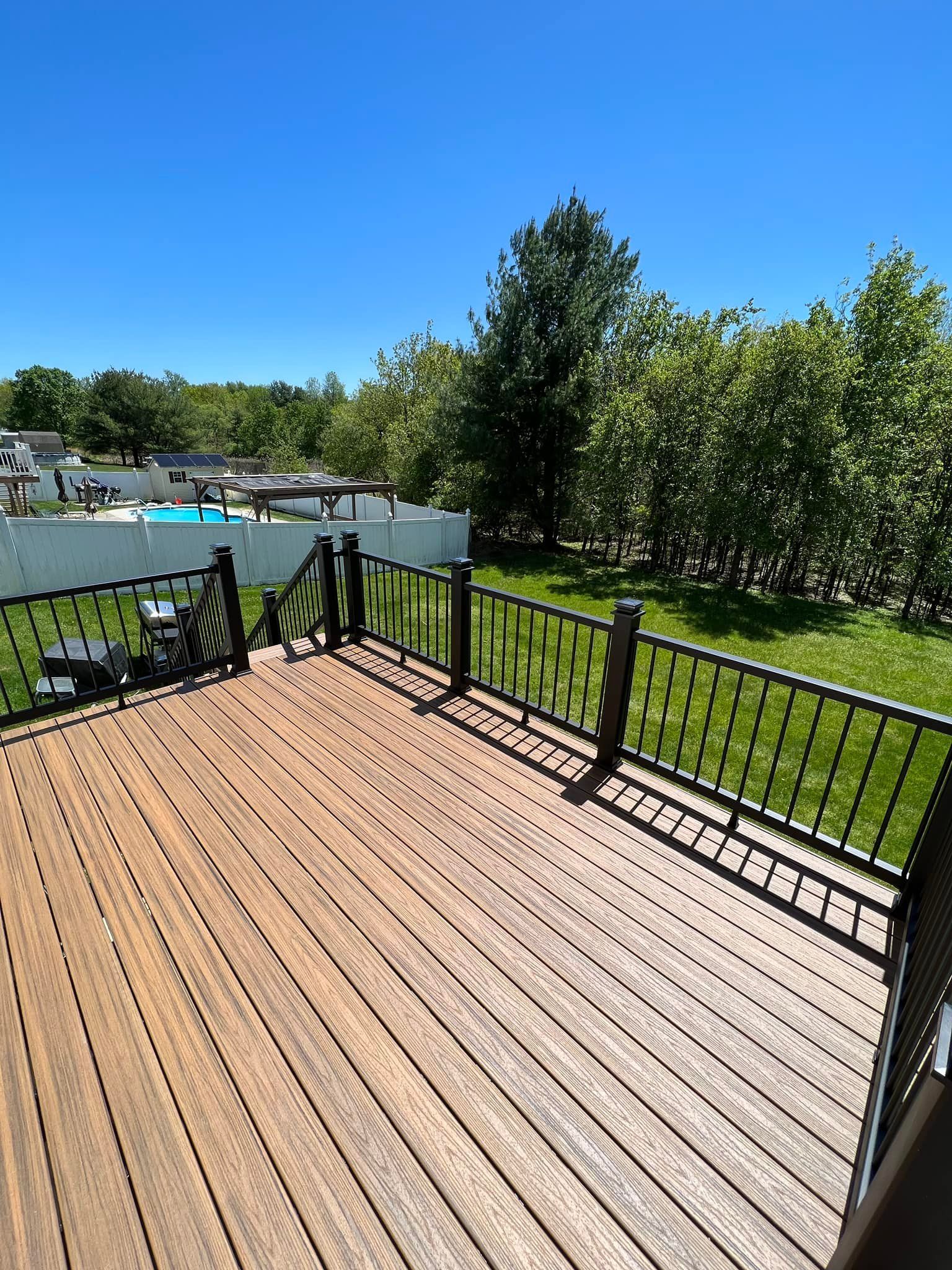 A wooden deck with a black railing overlooking a lush green field.