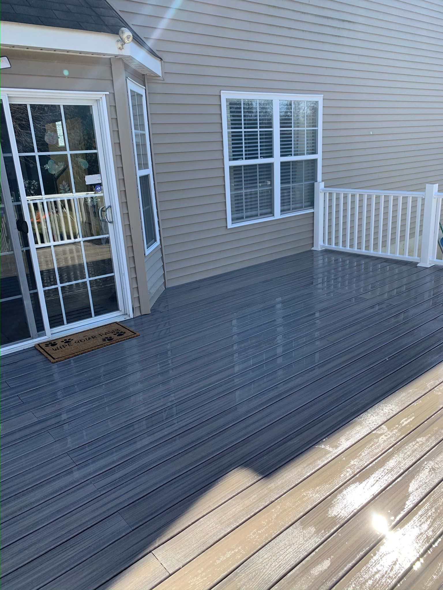 A deck with a sliding glass door and a white railing in front of a house.