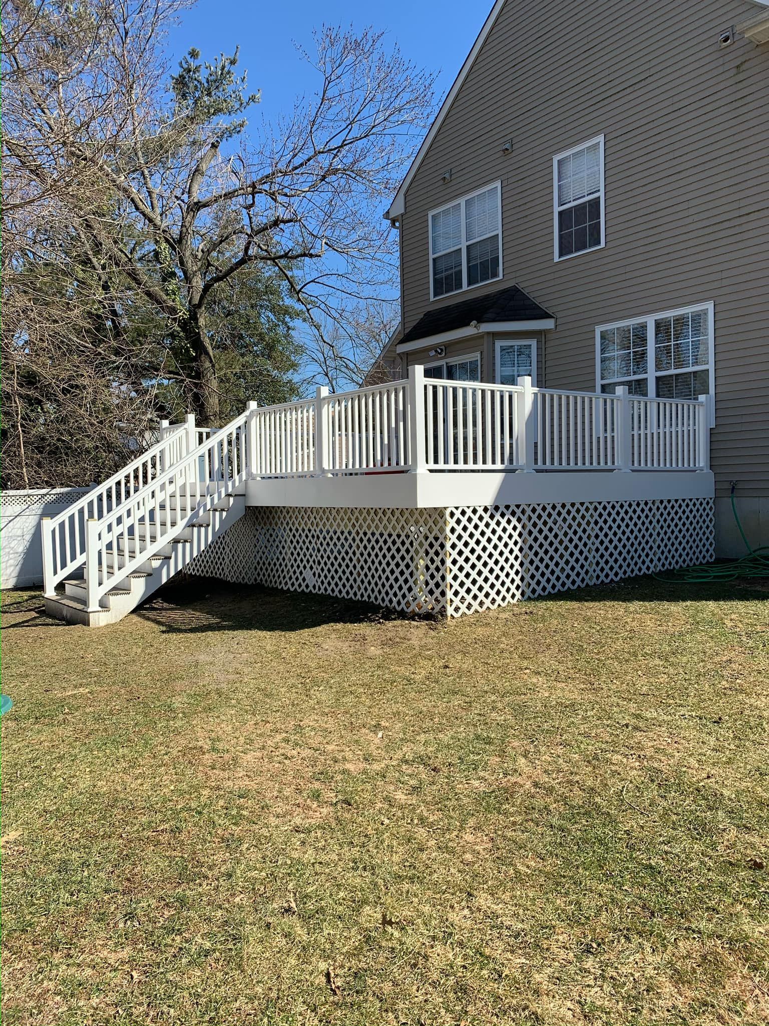 A large white deck with stairs is in the backyard of a house.