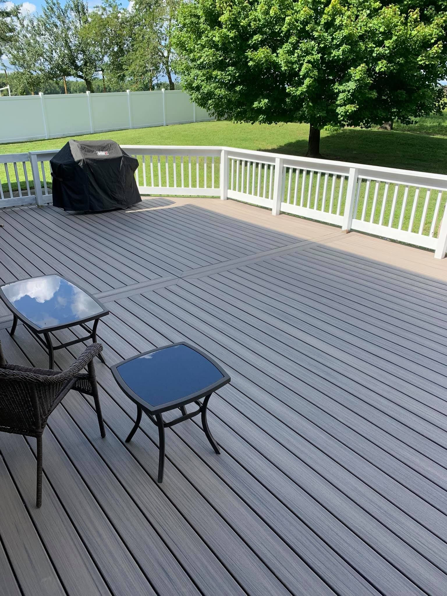A large wooden deck with a table and chairs and a grill.
