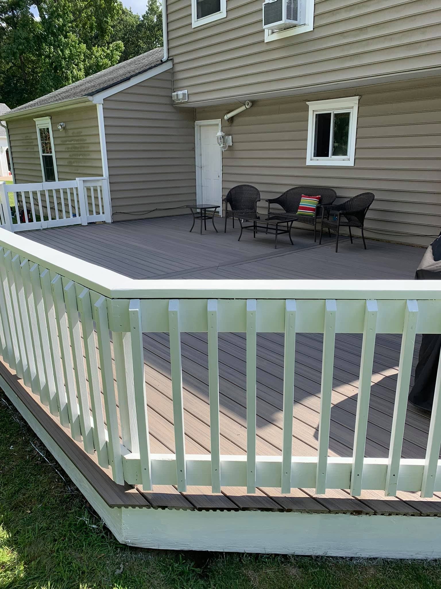 A large deck with a white railing and a house in the background.