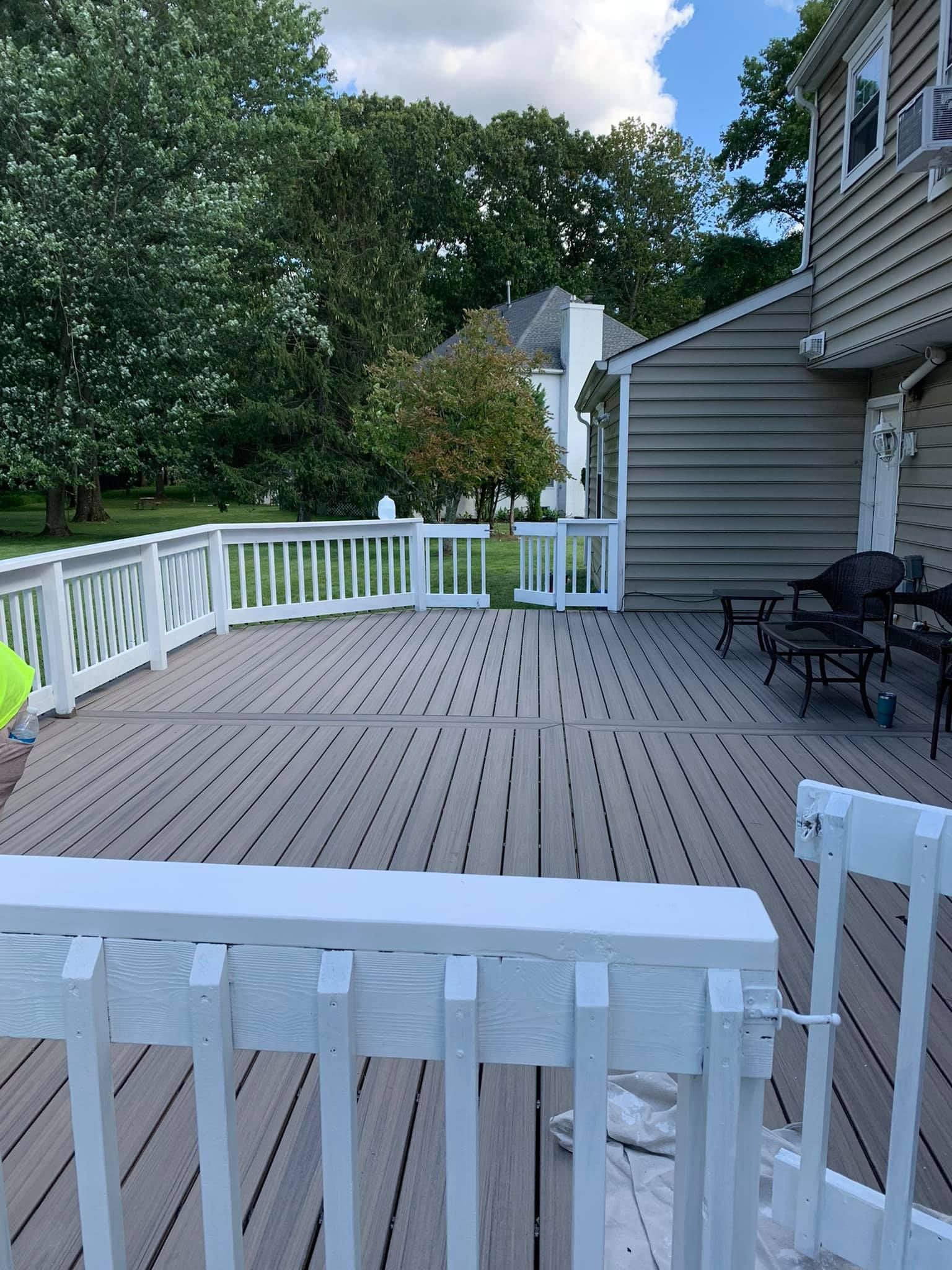 A large wooden deck with a white railing and a house in the background.