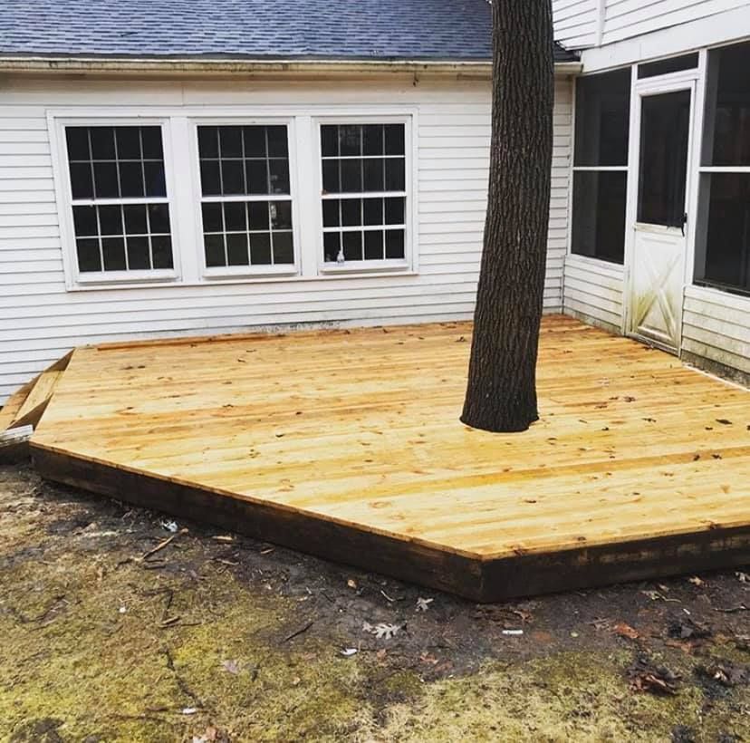 A wooden deck with a tree in the middle of it in front of a house.