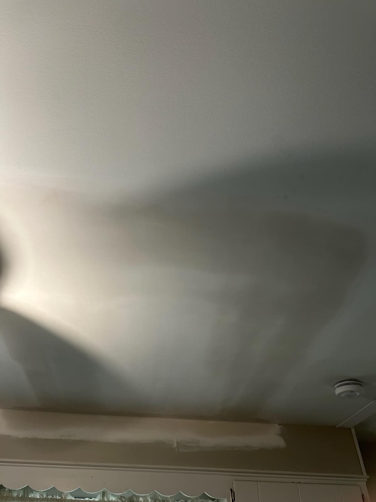 A ceiling fan is casting a shadow on the ceiling of a room.