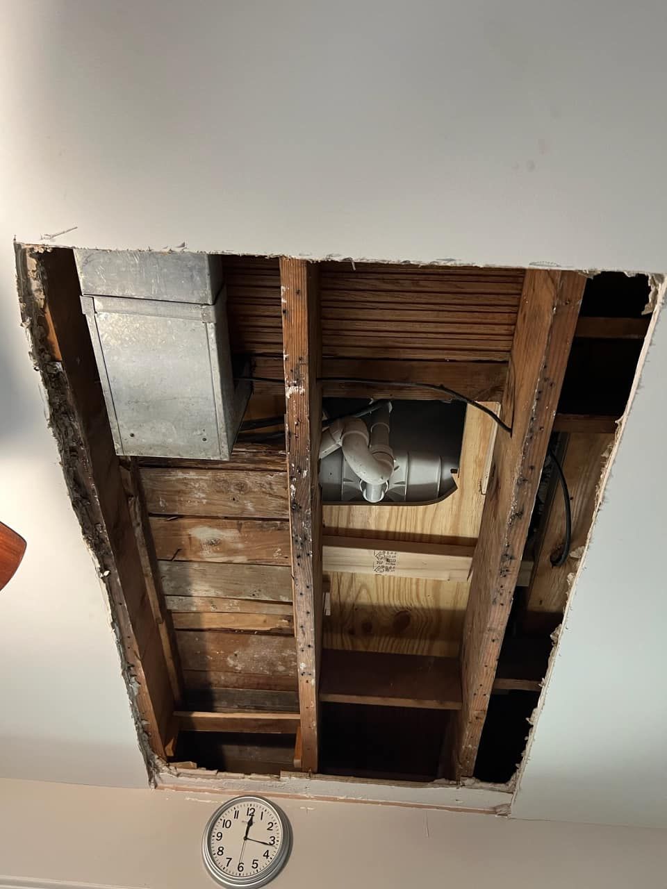 A ceiling with a hole in it and a clock on the wall.