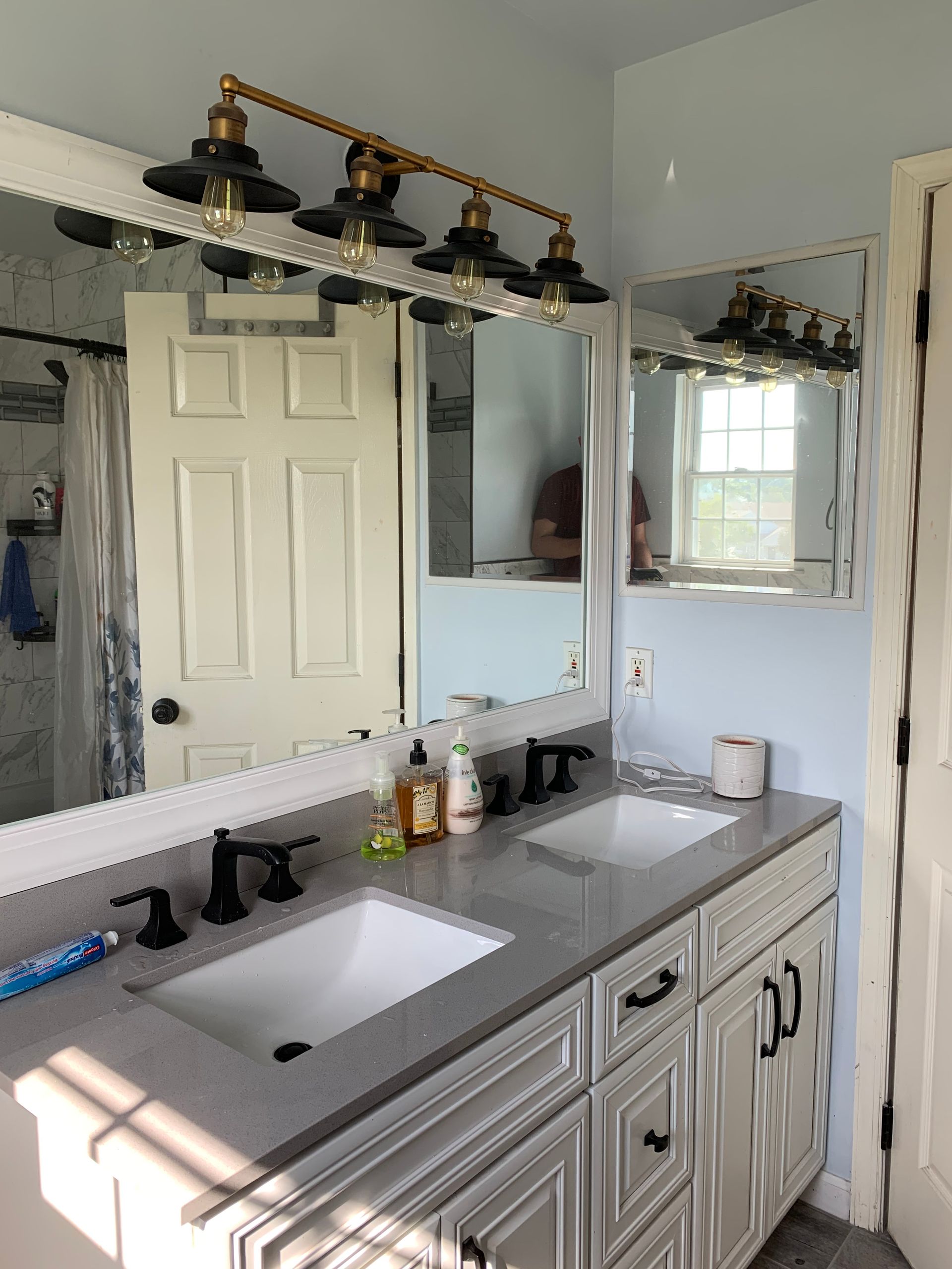 Bathroom vanity with double sinks, white cabinets, black faucets, and decorative lighting.