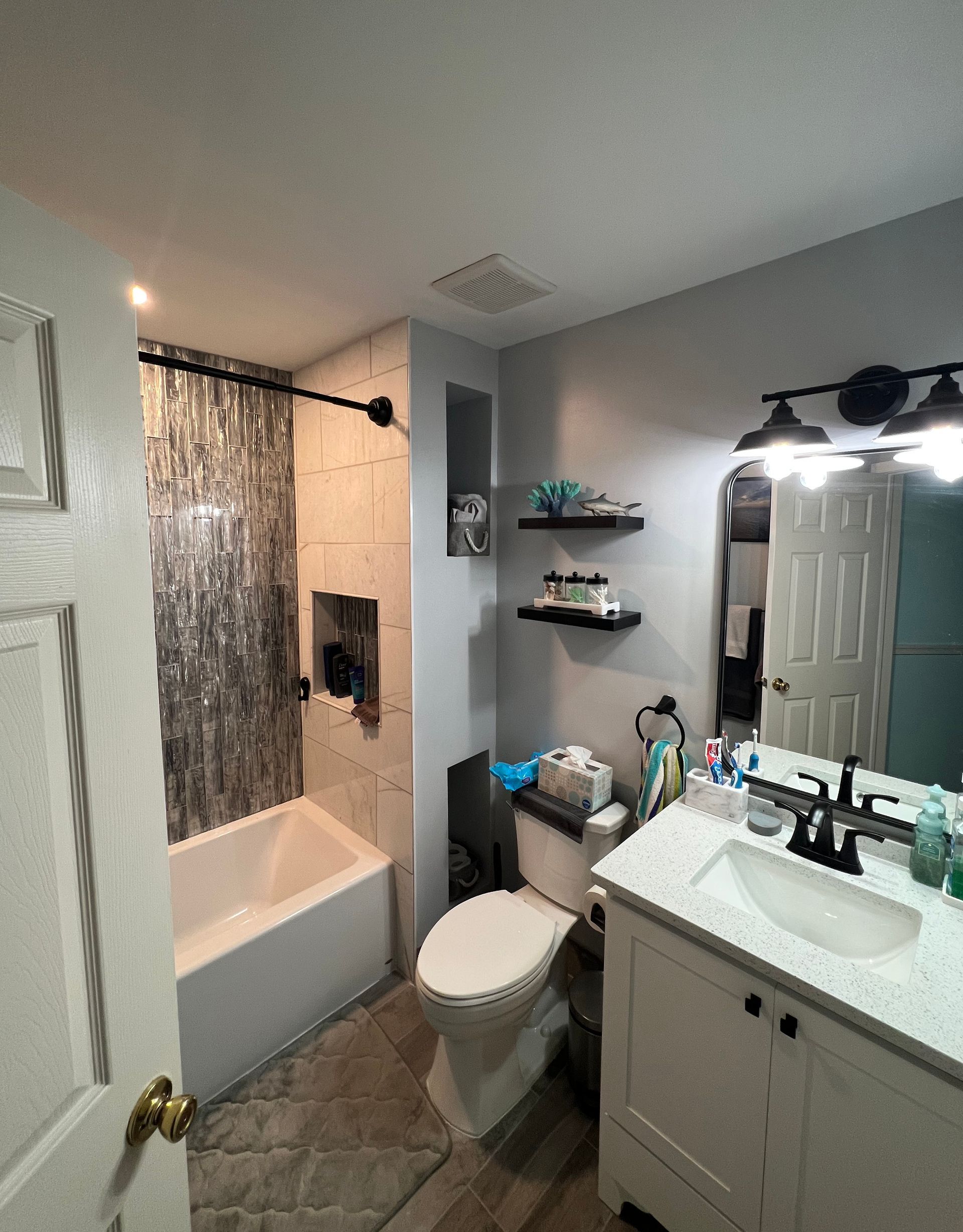 Bathroom with shower/tub, toilet, sink, and shelves. White and gray tile, blue walls, and a white vanity.