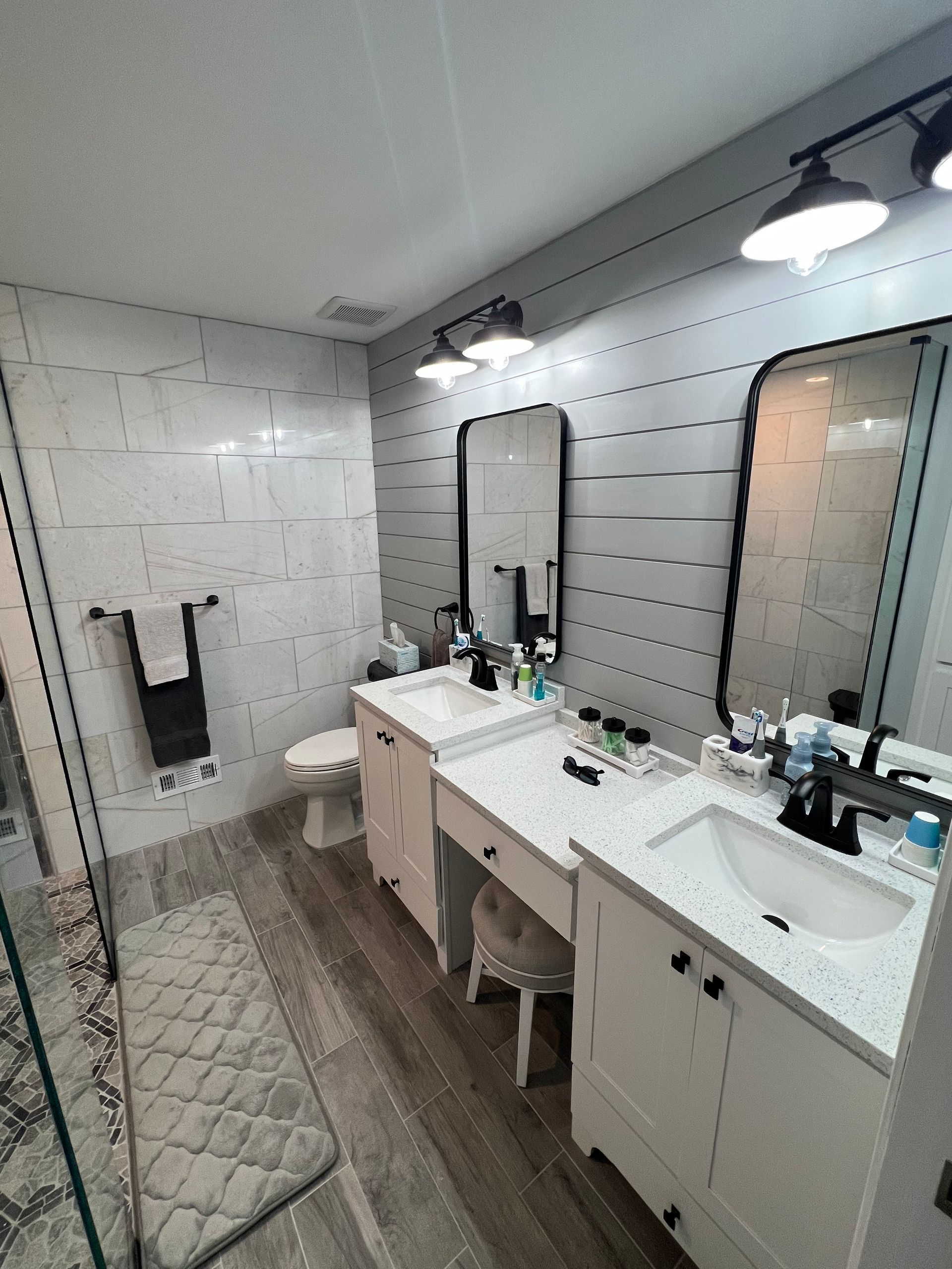 Bathroom with white cabinets, mirrors, and sink, gray tiled walls, a glass shower, and wood-look flooring.