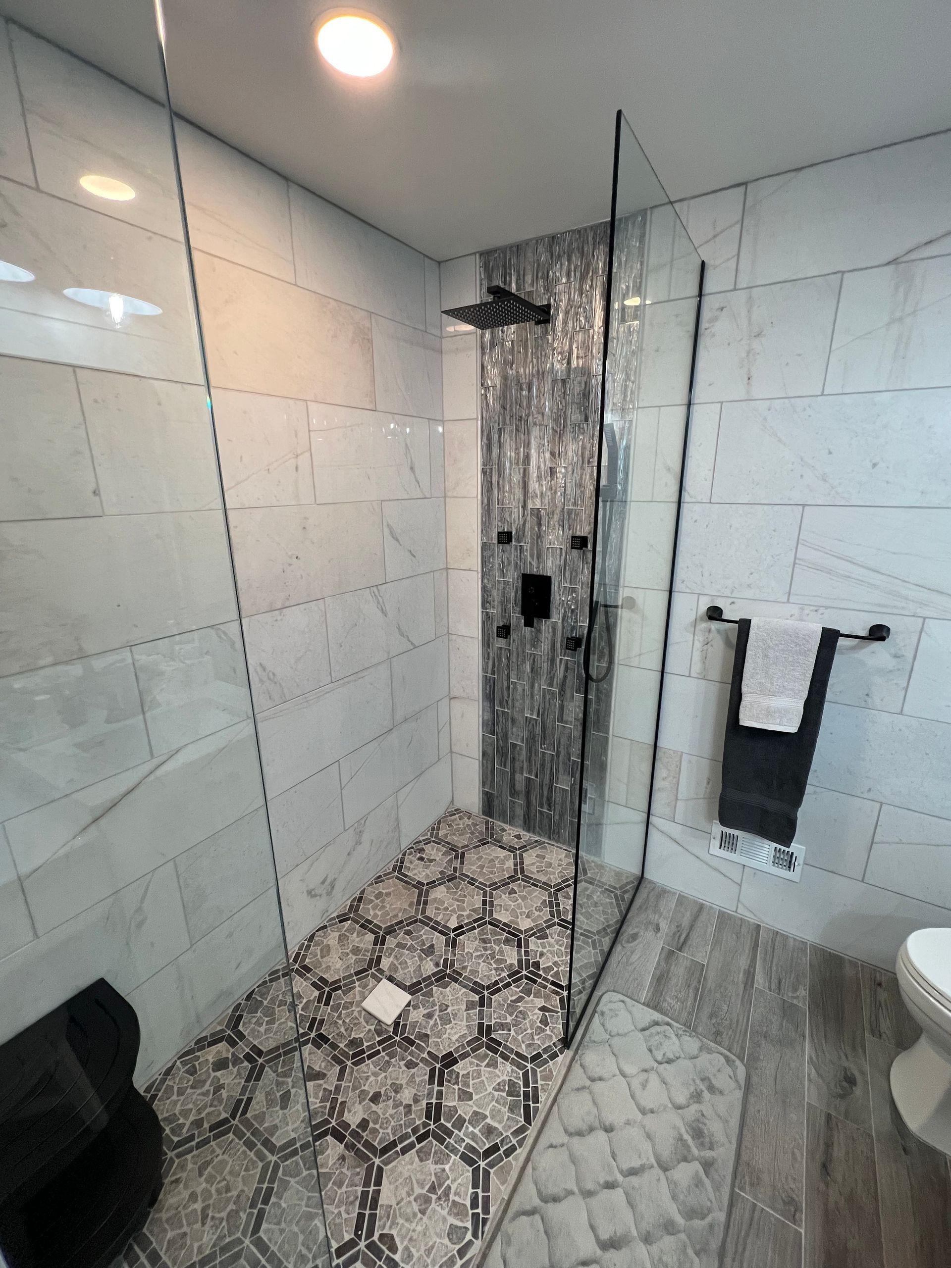 A modern bathroom with a tiled shower, a black towel rack, and a toilet.