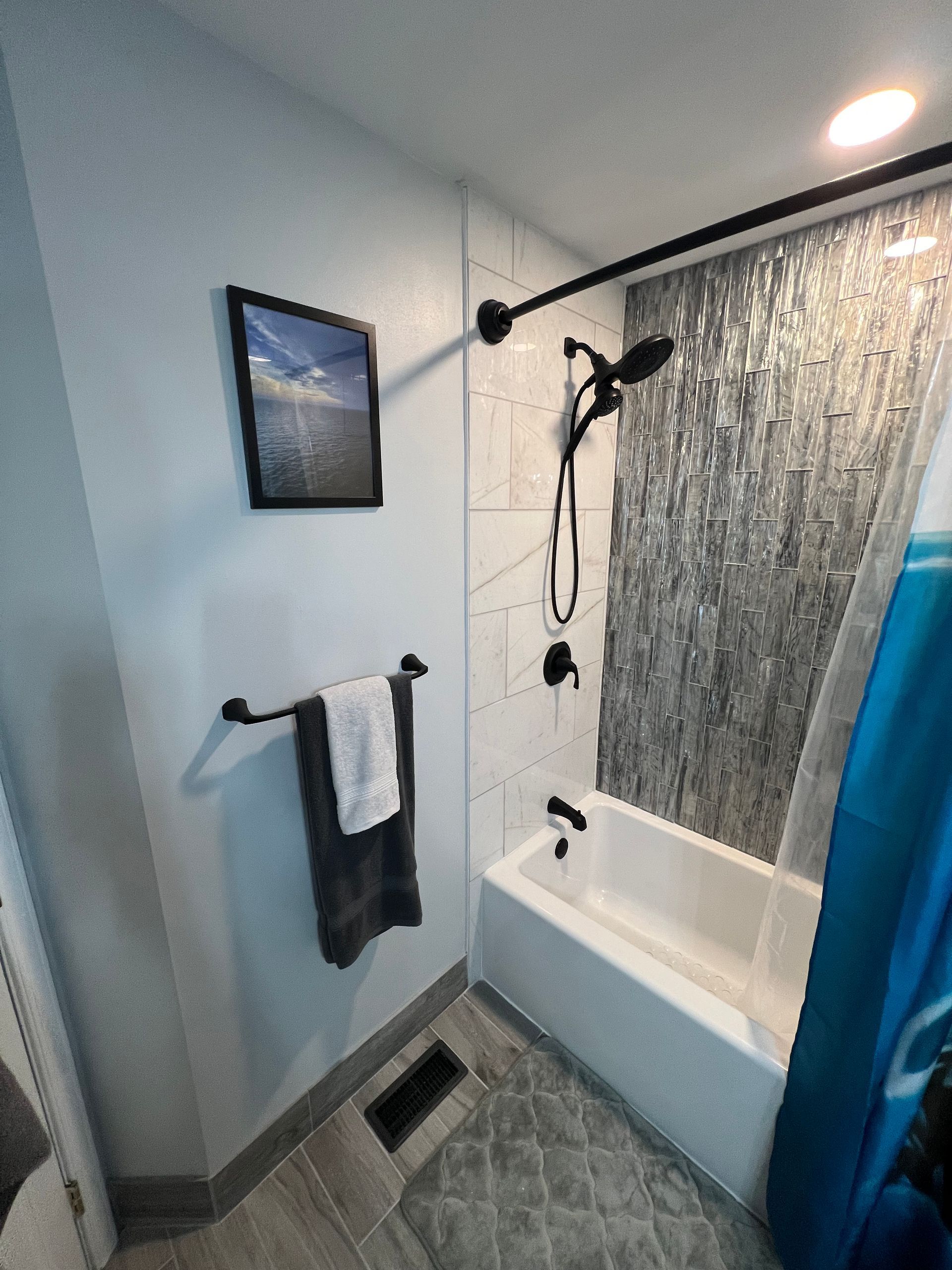 Bathroom with a tub and shower, black fixtures, decorative tile, and a framed picture.