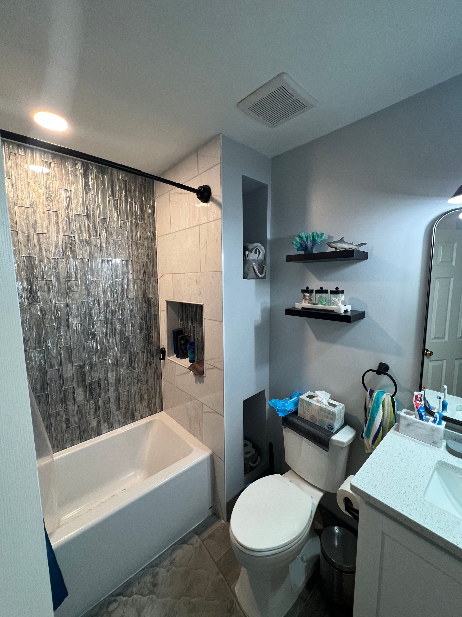 Bathroom with a white tub, gray stone accent wall, toilet, and shelving.