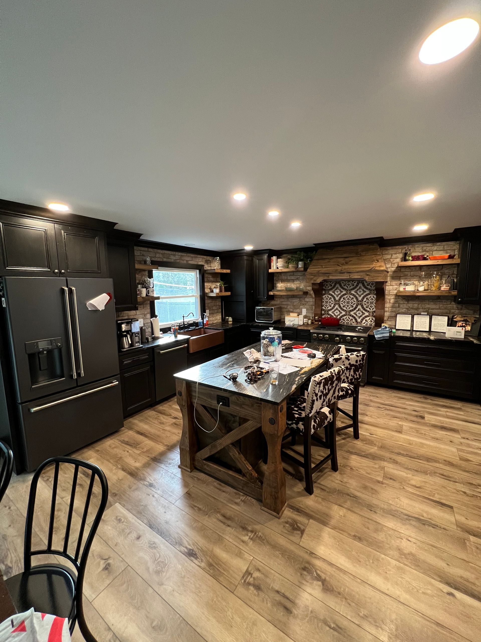 Rustic kitchen with dark cabinets, wood island, brick accent wall, and light wood floors.