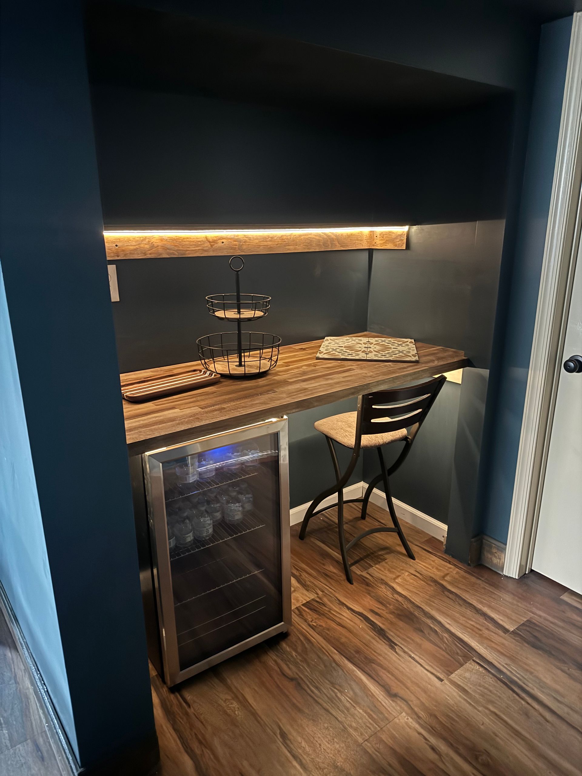 A small home bar nook with a dark countertop, a wine fridge, and a stool.
