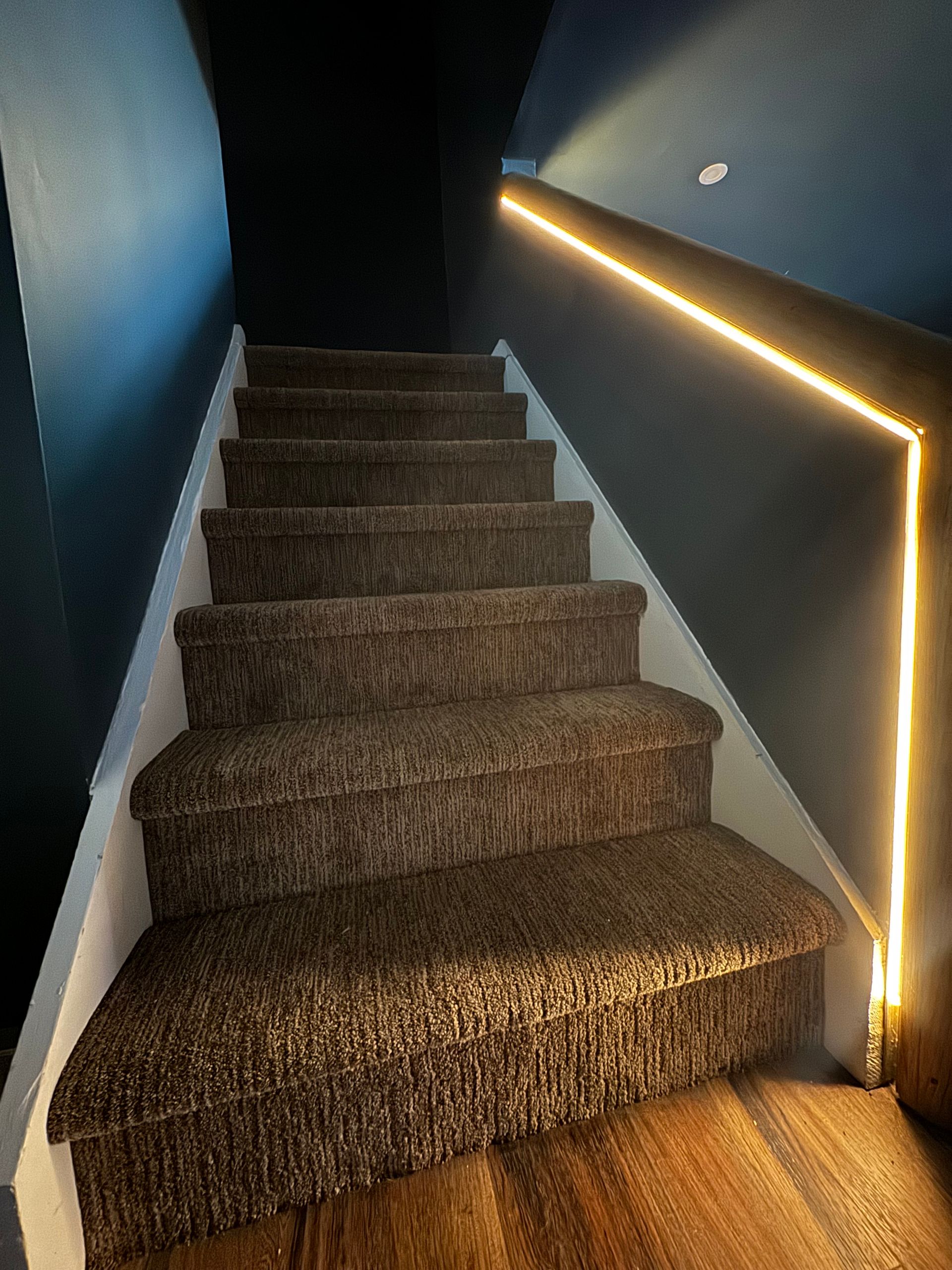 Staircase with brown carpet and LED lighting on the wall.