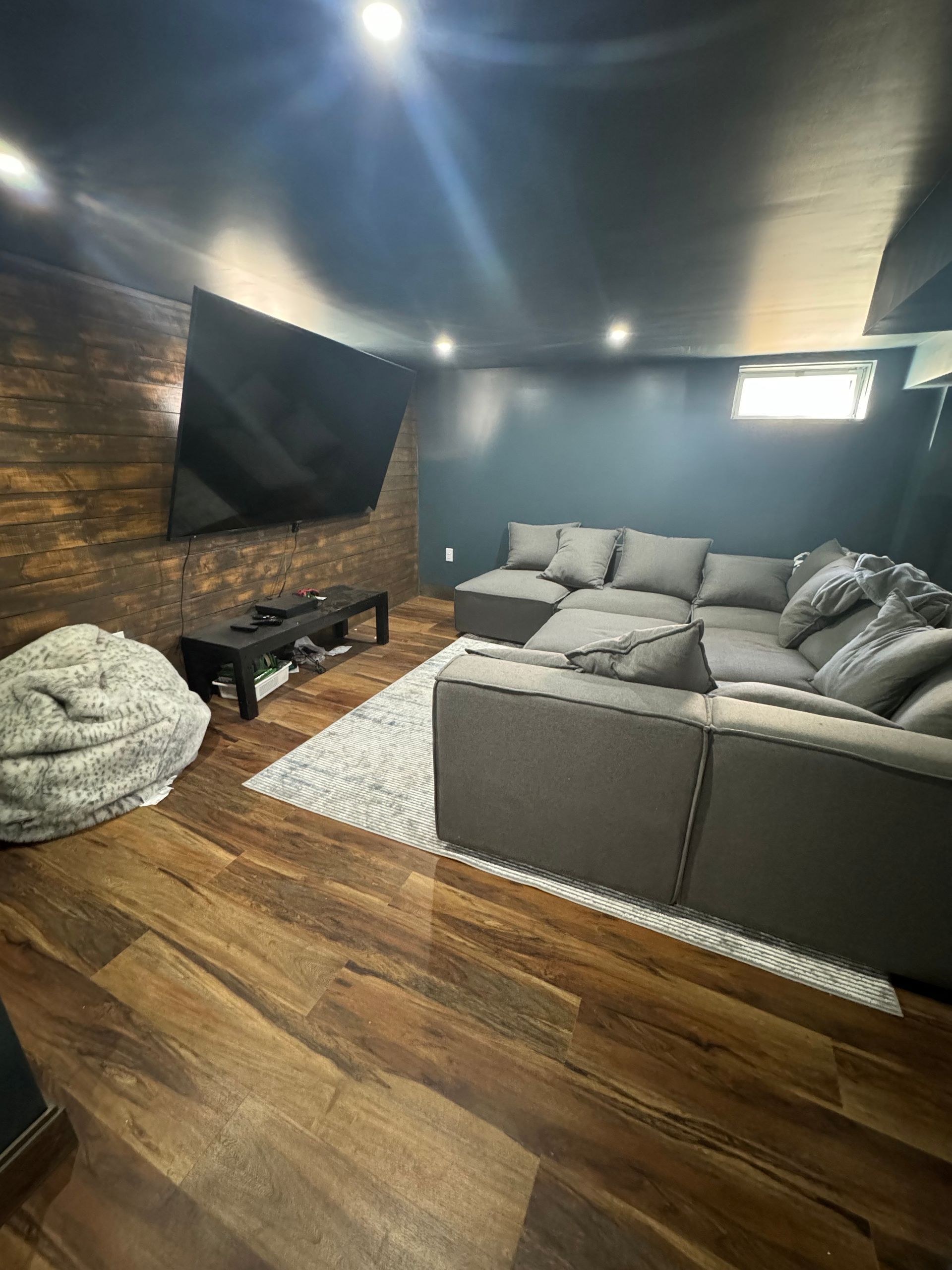 Cozy basement entertainment area with dark walls, sectional sofa, TV, and wood accent wall.