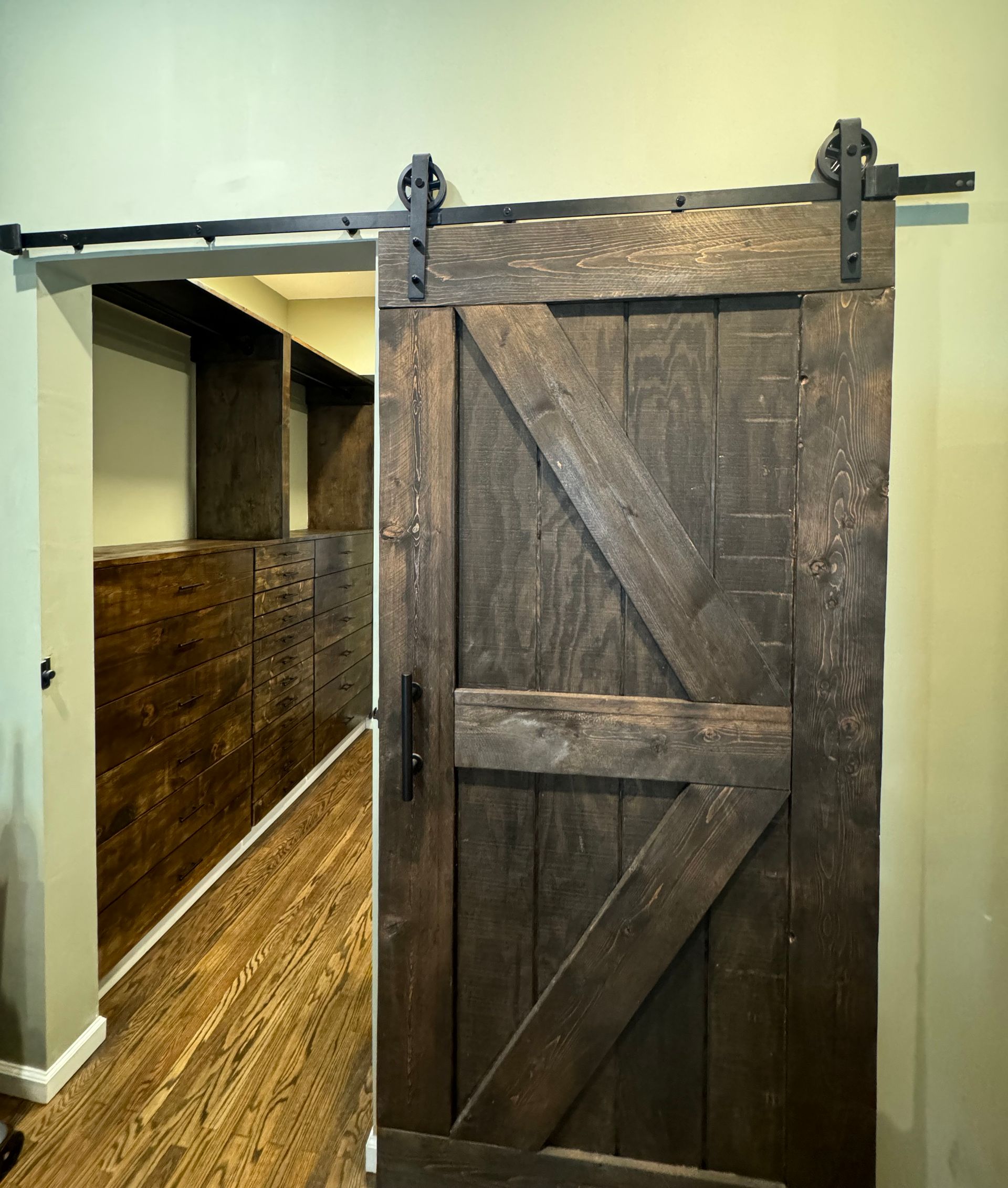 Rustic barn door, dark wood, sliding open to a hallway with wooden walls and floor.