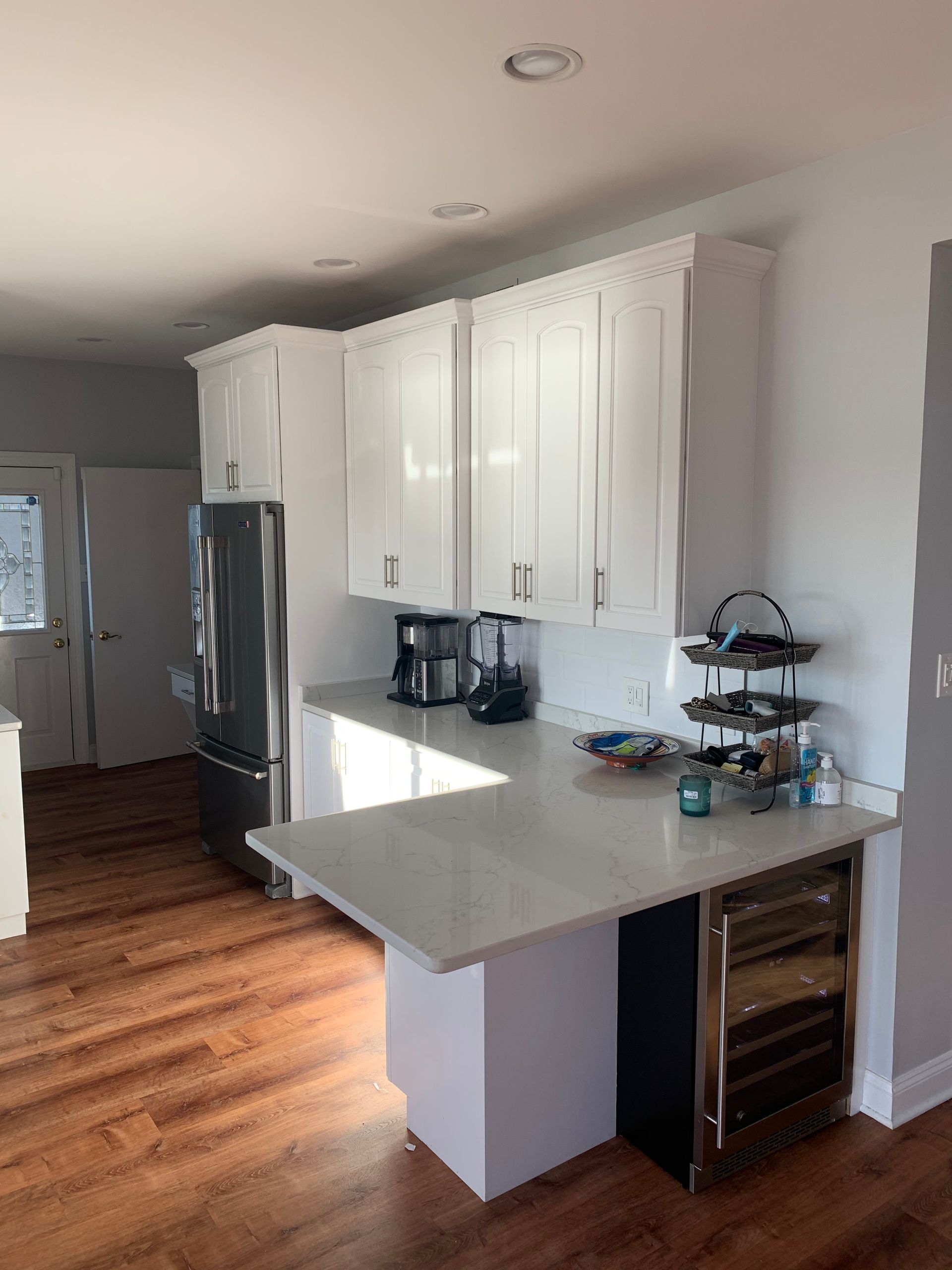 White kitchen with wood floor, countertop, cabinets, refrigerator, wine cooler.