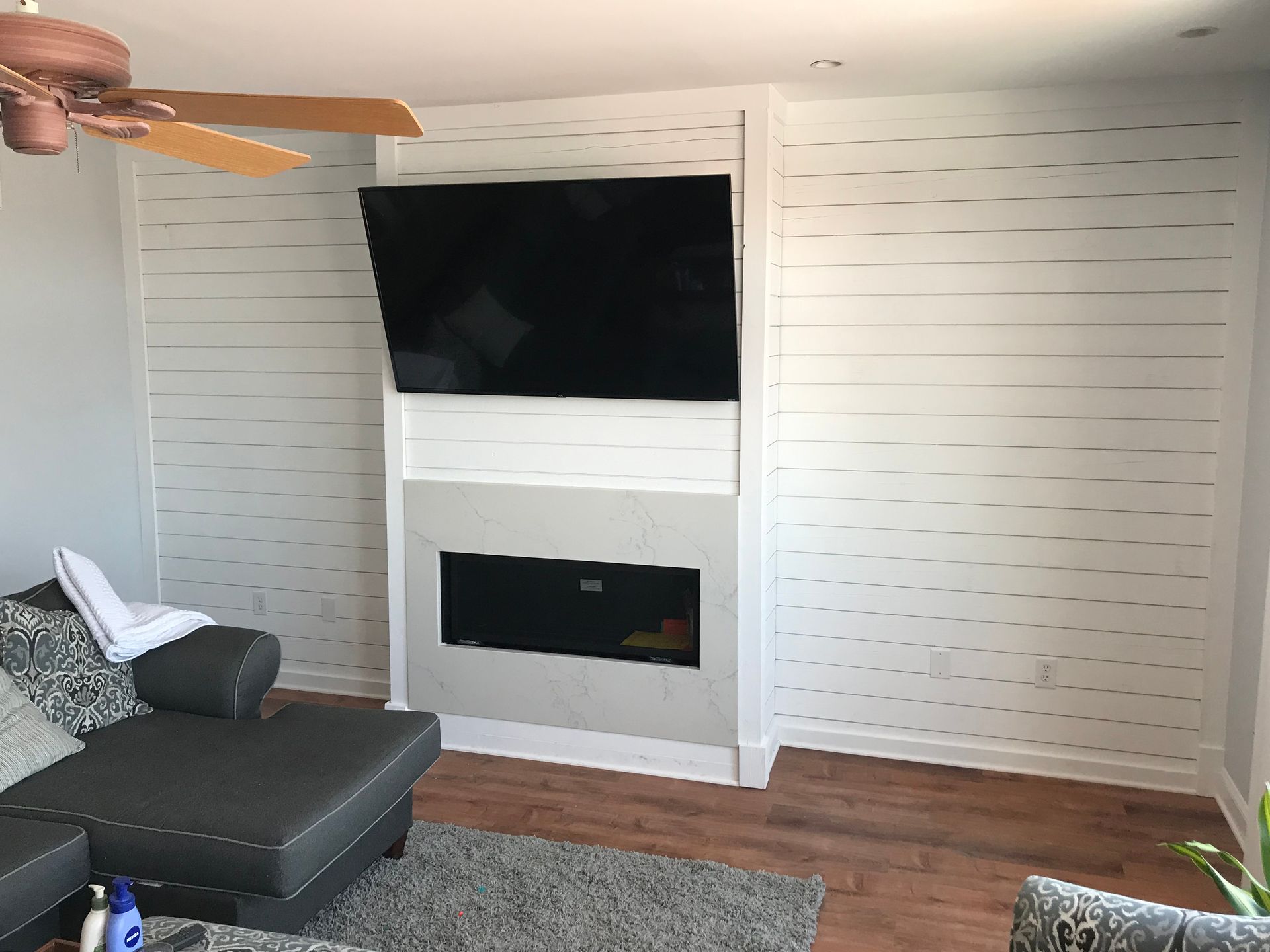 Living room with white shiplap wall, mounted TV above a fireplace, and a gray sectional sofa.