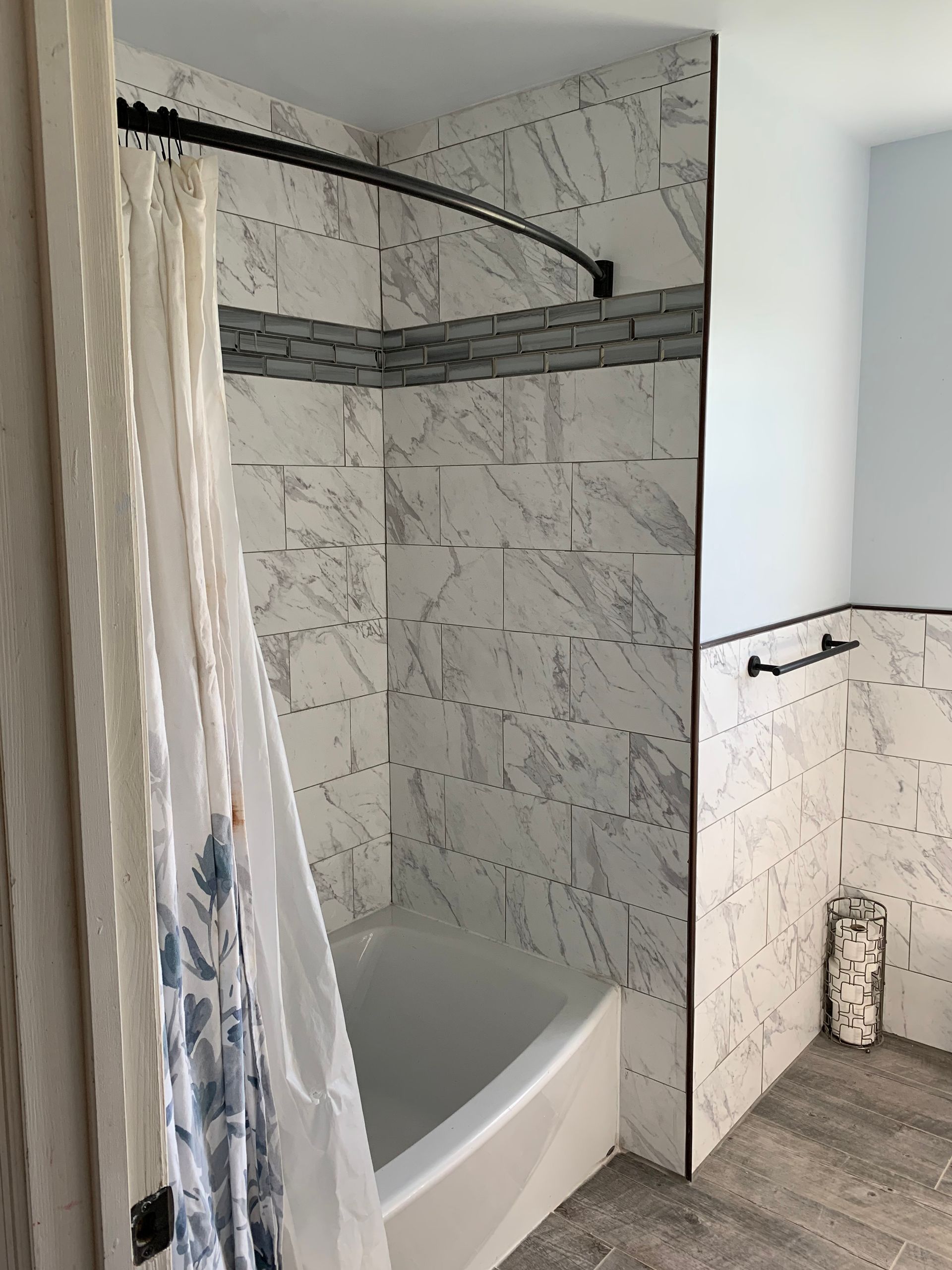 Bathroom with white marble tile walls, curved shower rod, and a blue and white shower curtain.
