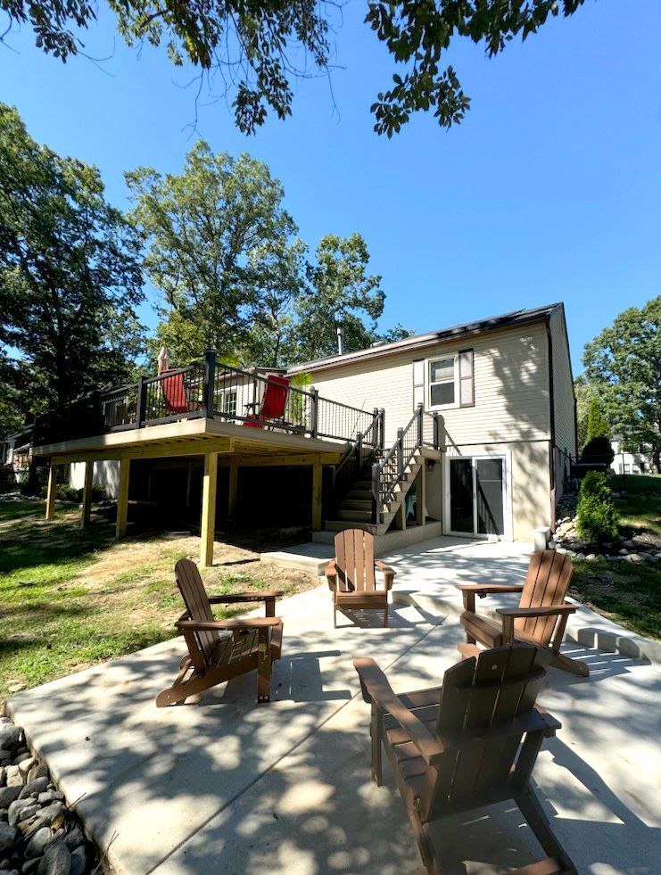 Backyard patio with wooden chairs facing a house with a deck. Blue sky.