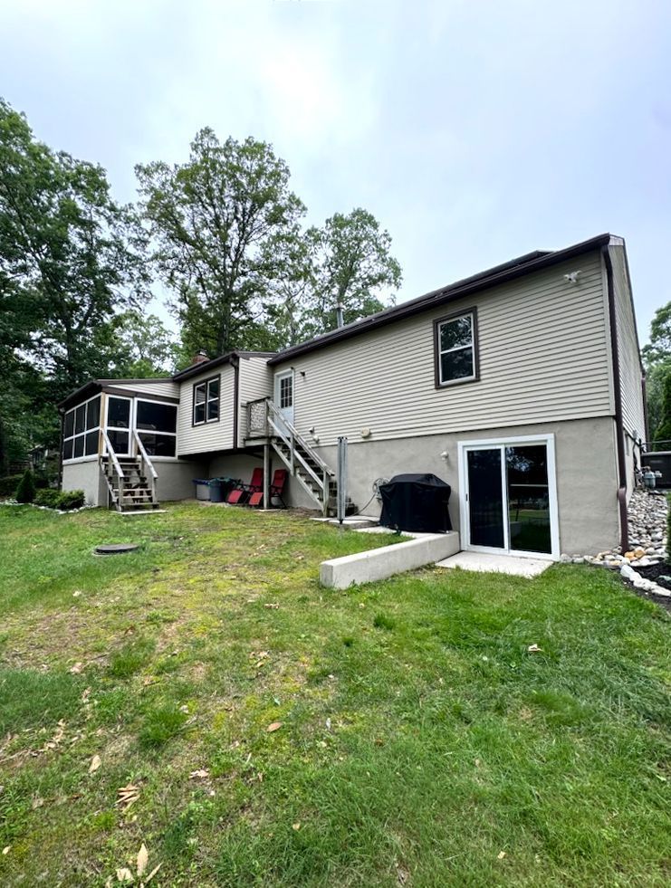 Back of a beige house with a screened porch, wooden stairs, and a grassy yard.