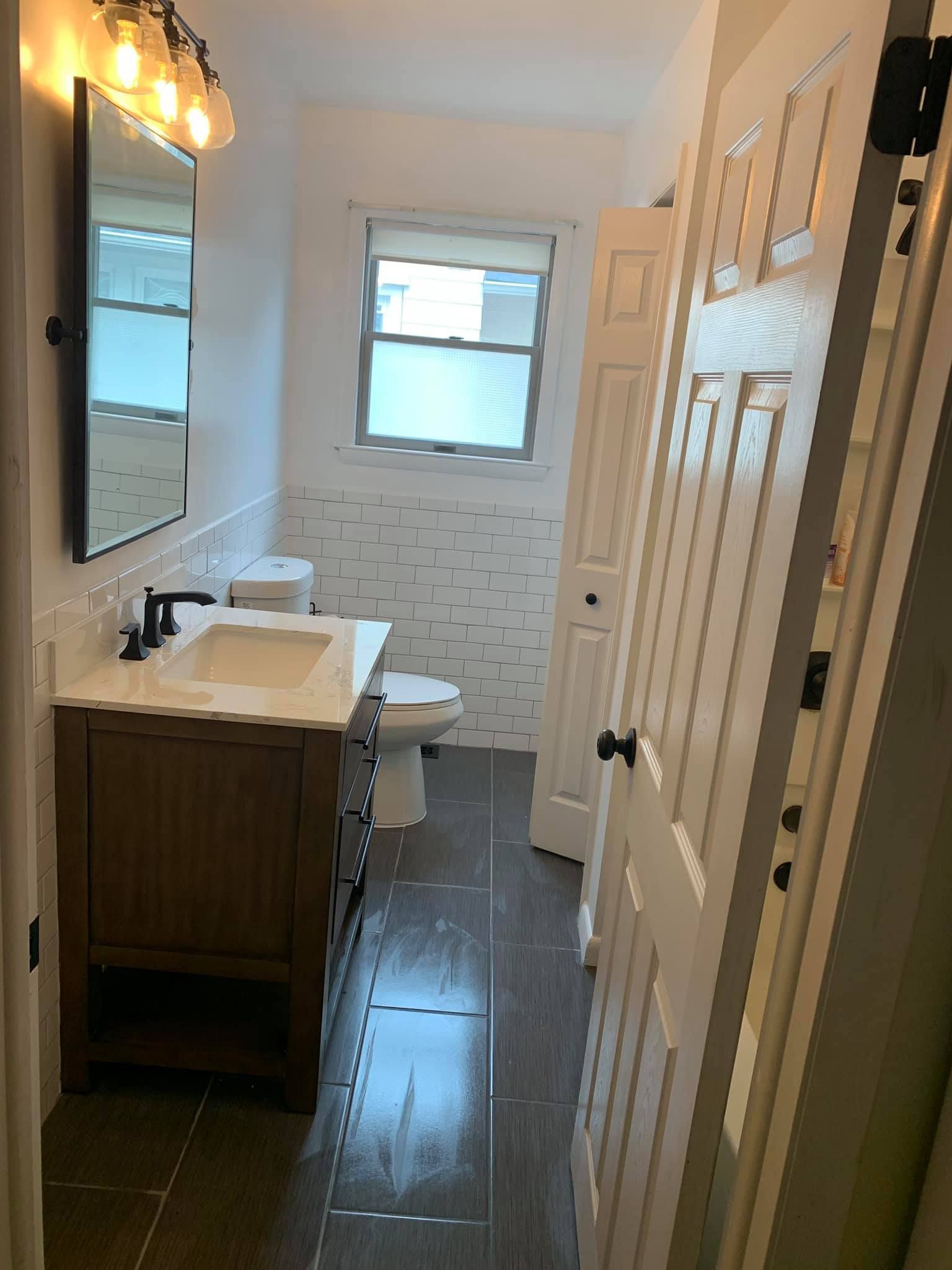A bathroom with a sink , toilet , mirror and window.