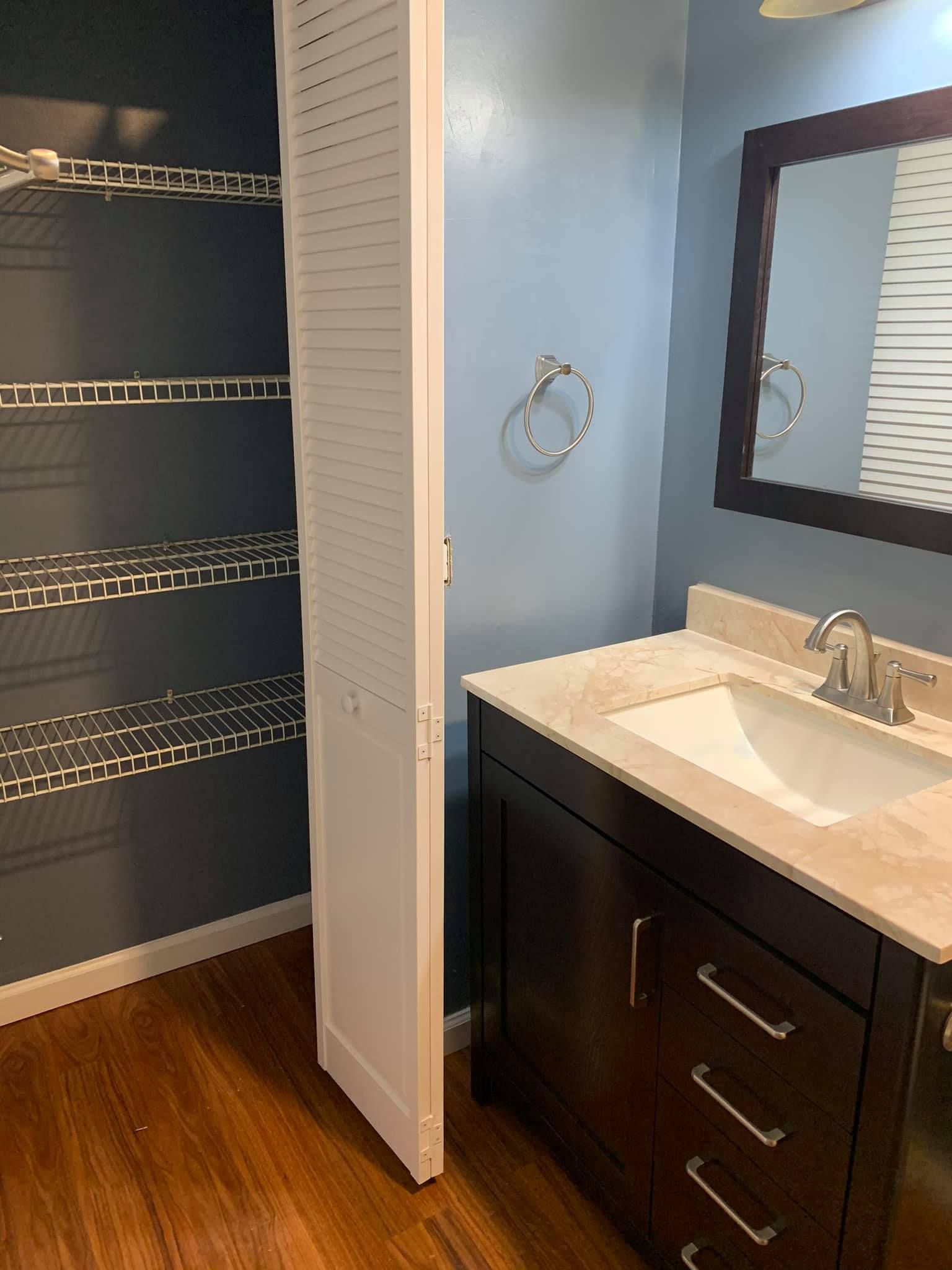 A bathroom with a sink , mirror and closet.