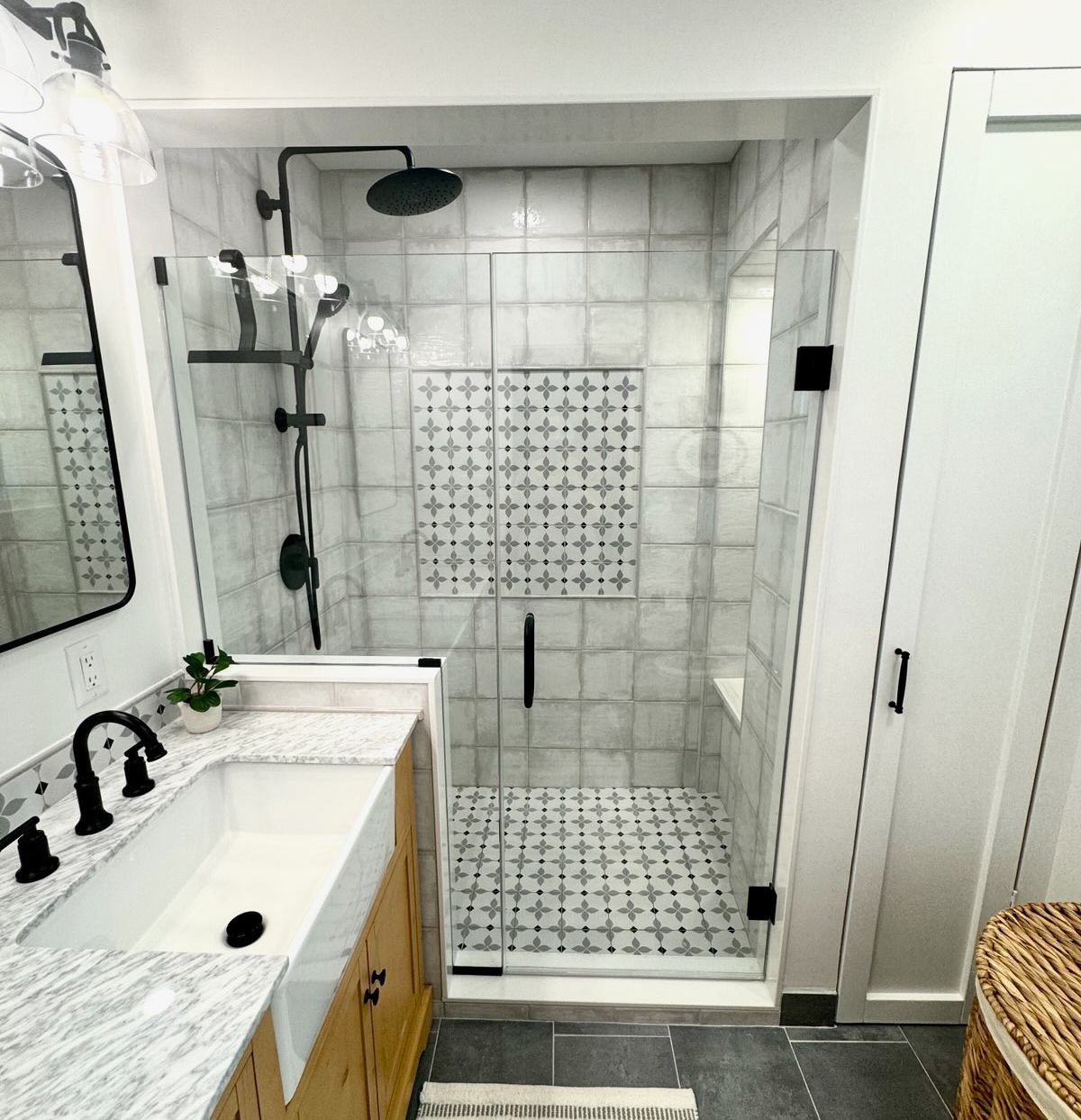 Bathroom with a walk-in shower, light tiles, black fixtures, white sink, and light wood cabinet.