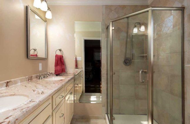 Bathroom with cream cabinets, granite countertops, glass shower, and beige walls.