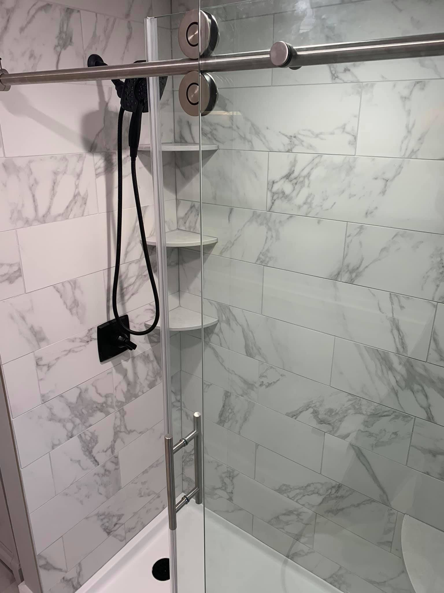 A shower stall with a sliding glass door and a shower head.