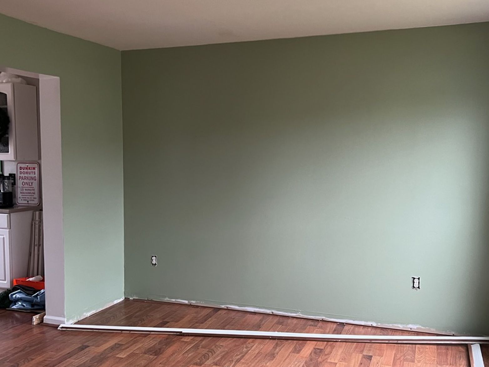 Green painted room with hardwood floor, electrical outlets, and white trim.