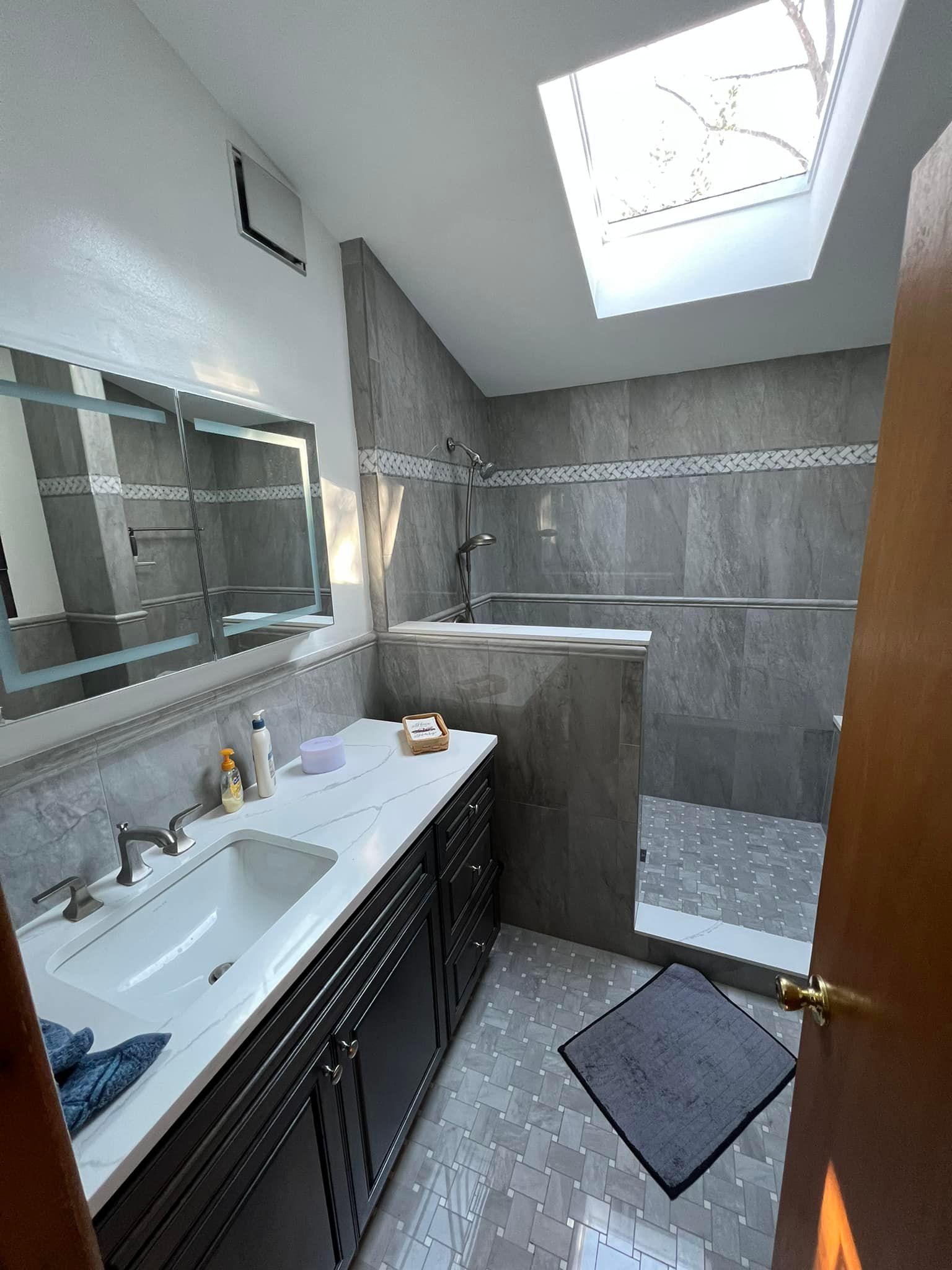 A bathroom with a sink , mirror , tub and skylight.