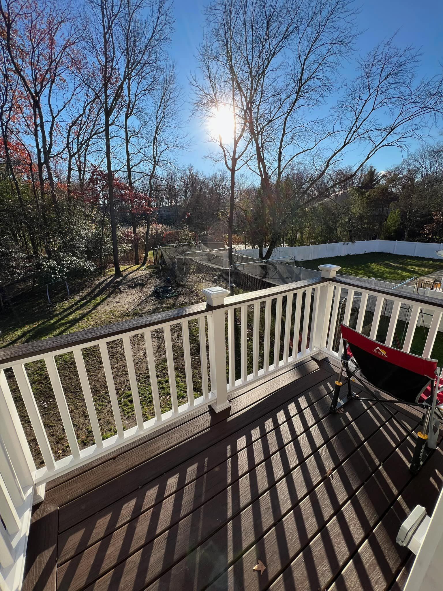 A deck with a white railing and a red chair on it.