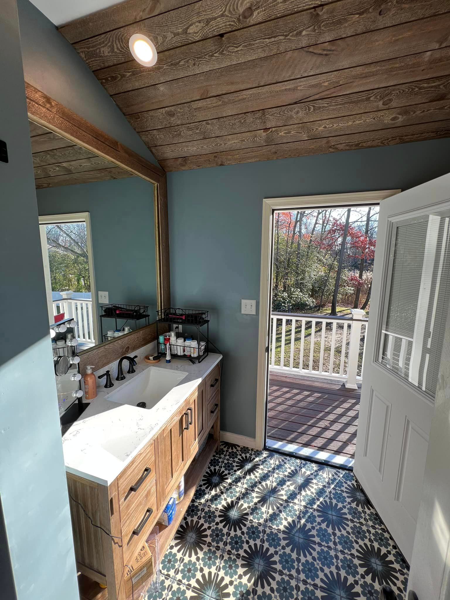 A bathroom with a sink , mirror , and door leading to a balcony.