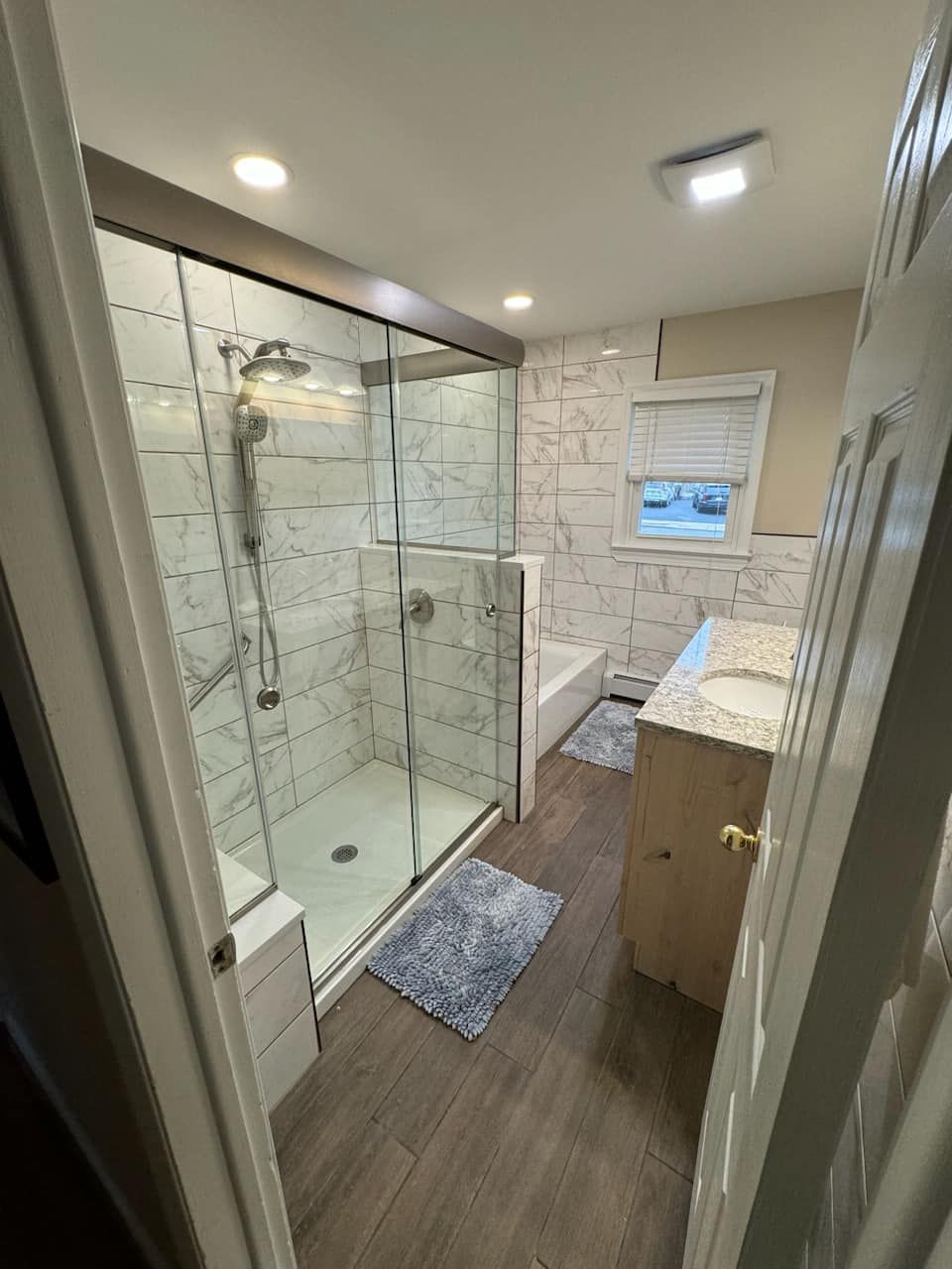 A bathroom with a walk in shower , tub , sink and window.