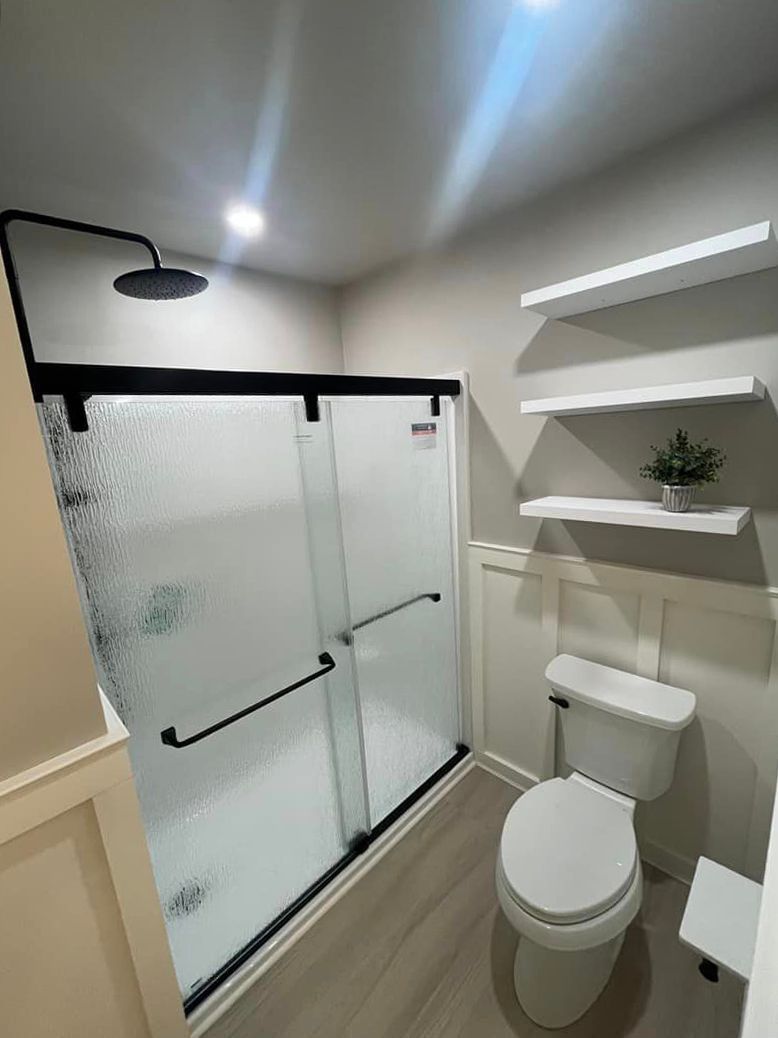 A bathroom with a toilet , shower , and shelves.