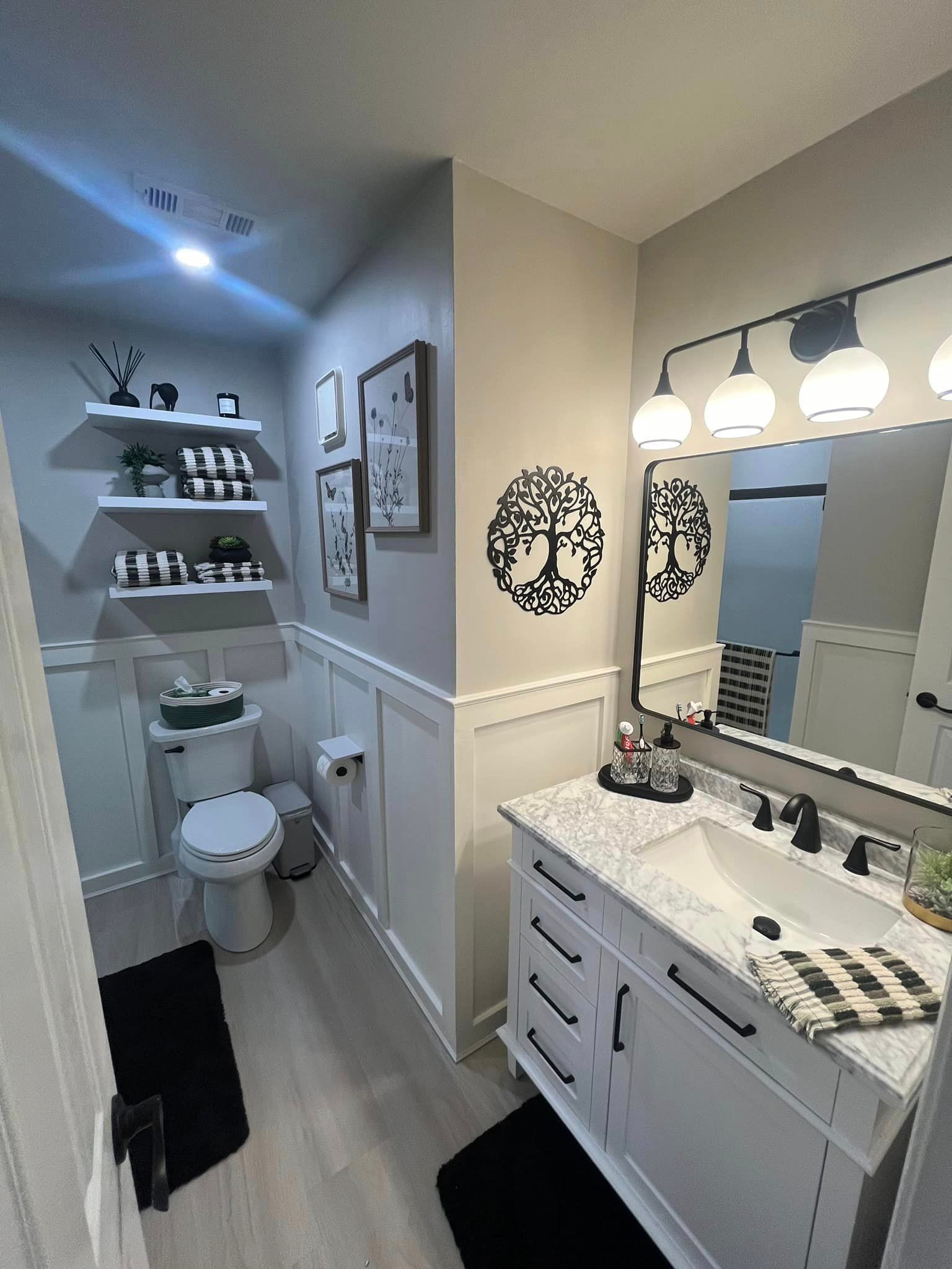 A bathroom with a toilet , sink , mirror and shelves.