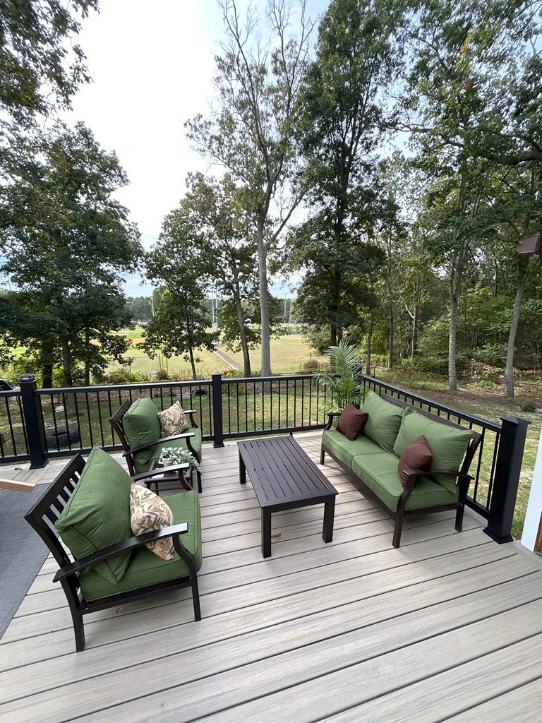 Outdoor deck with green cushions on dark furniture, looking over a field.