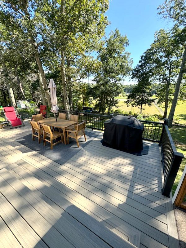 Outdoor deck with dining table, chairs, and grill, overlooking green field.