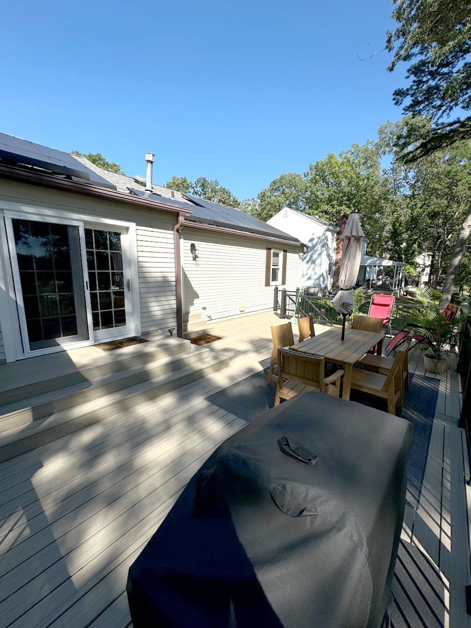 Deck with covered grill, table and chairs, and a house with solar panels on a sunny day.